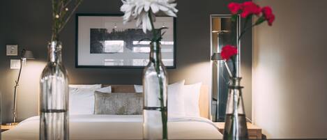 A hotel room with a bed, two vases with flowers, a framed picture on the wall, and a mirror.