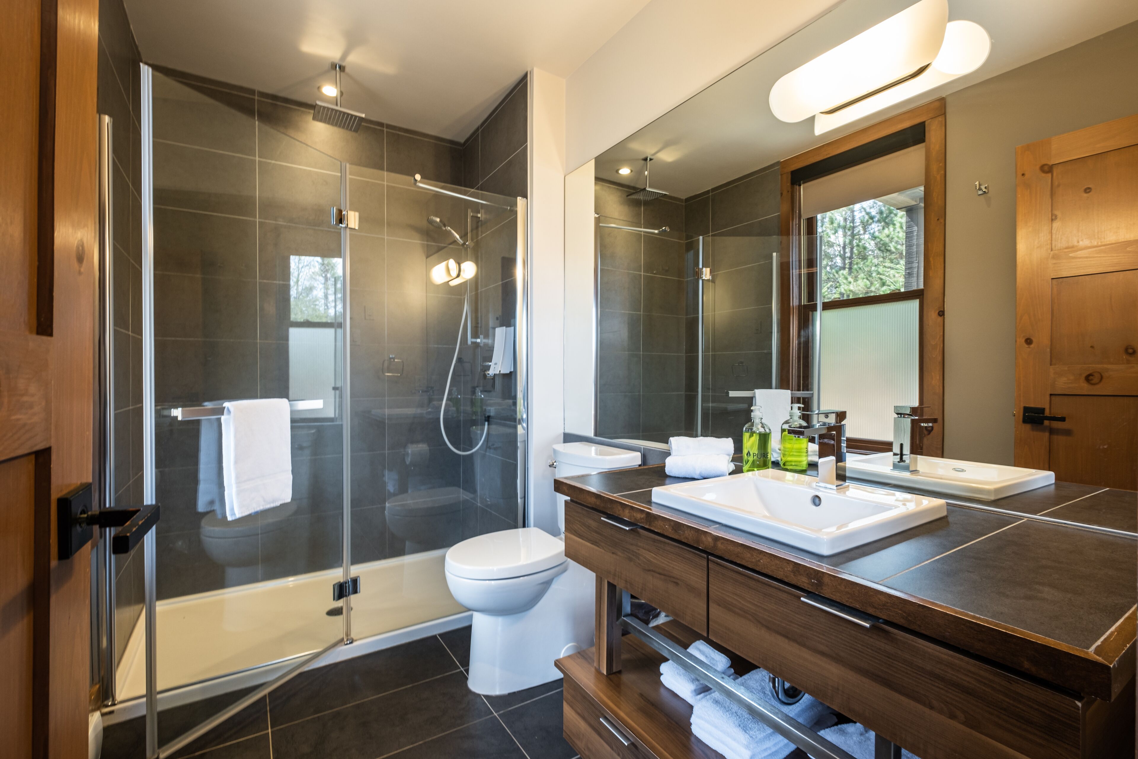Une salle de bain moderne avec une douche à parois de verre, des toilettes blanches et un meuble-lavabo en bois avec un miroir.