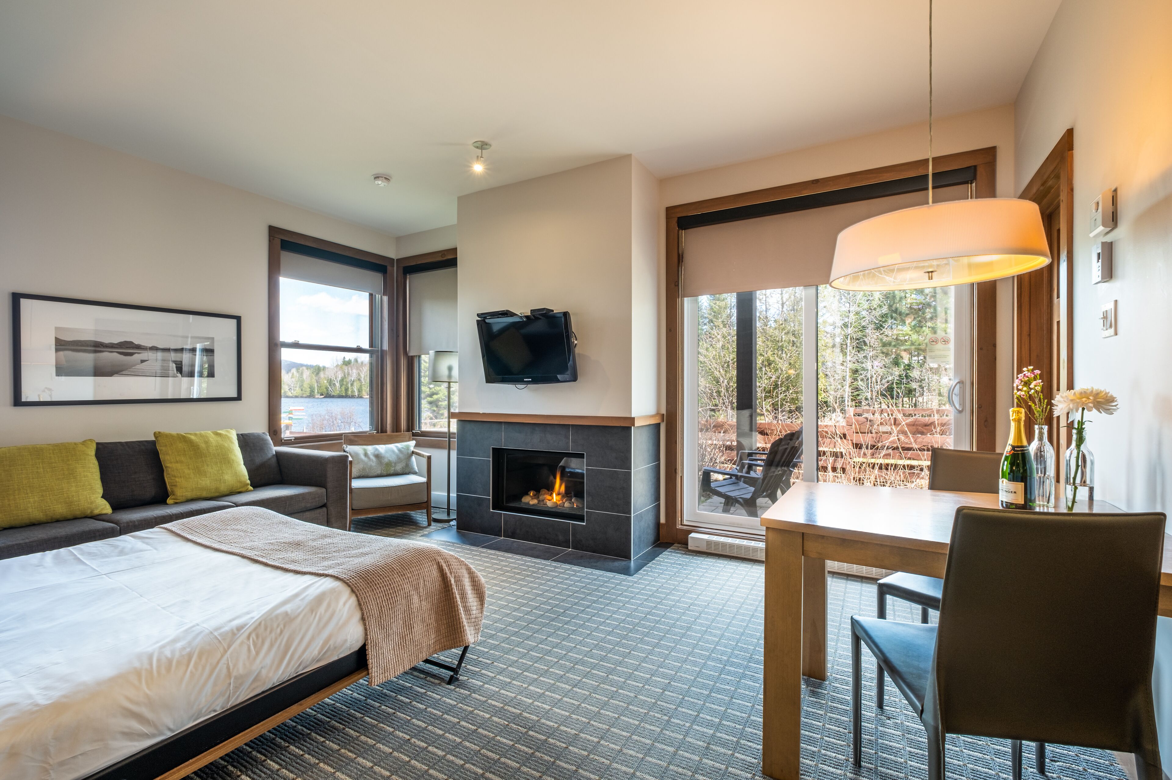 A modern hotel room with a large bed, a fireplace, a dining table, and a TV mounted on the wall.