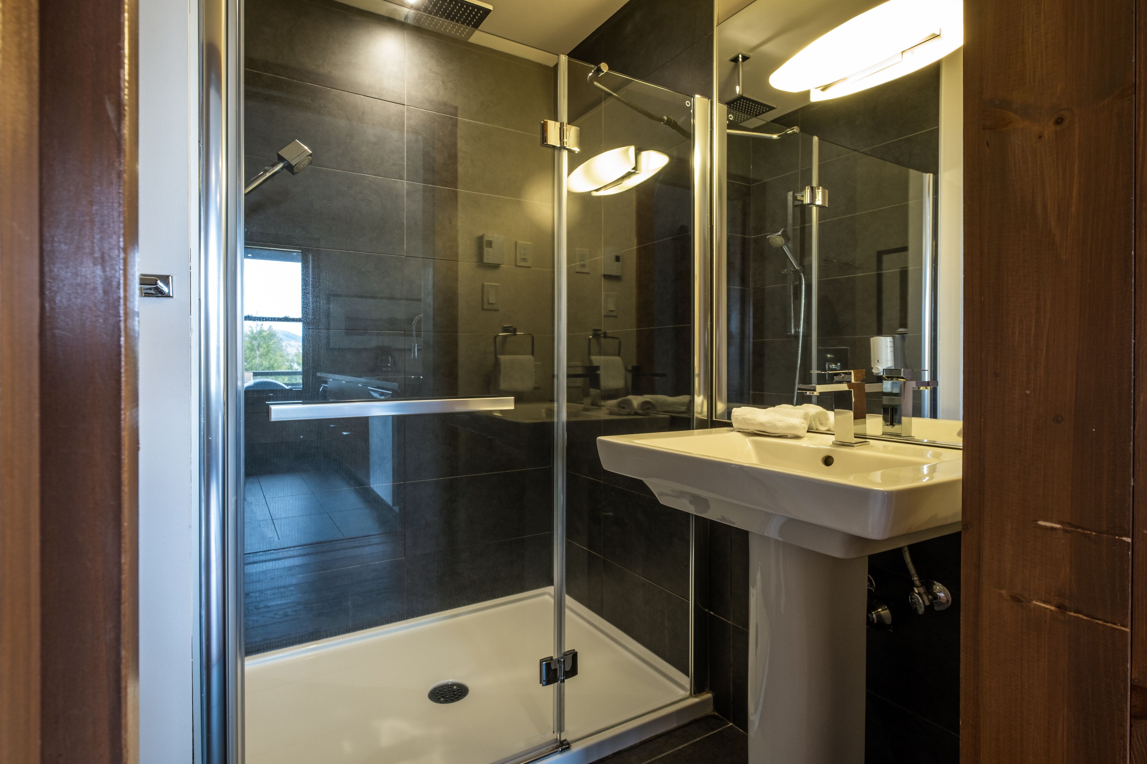 A modern bathroom with a glass-enclosed shower, a white sink, and a large mirror.