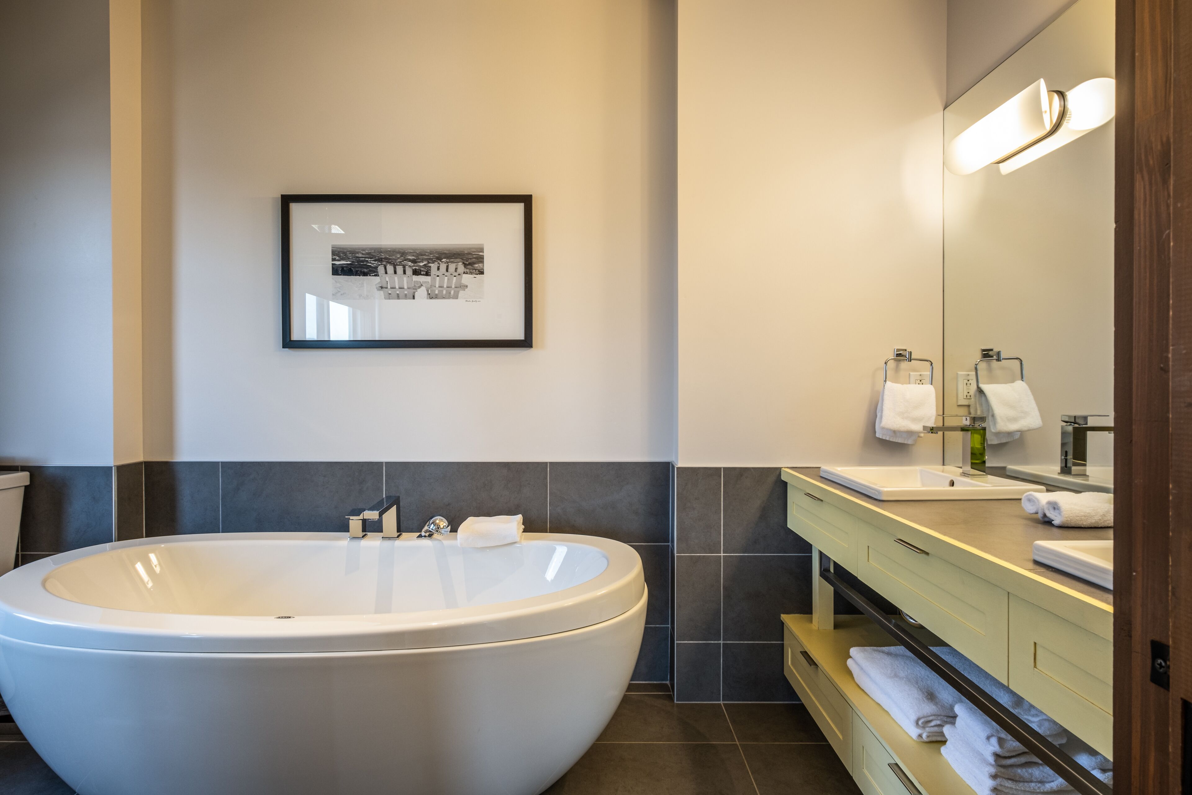 Ein modernes Badezimmer mit einer großzügigen, freistehenden Badewanne, einem gerahmten Bild an der Wand und einem Waschtisch mit Spiegel und Handtuchhalter.