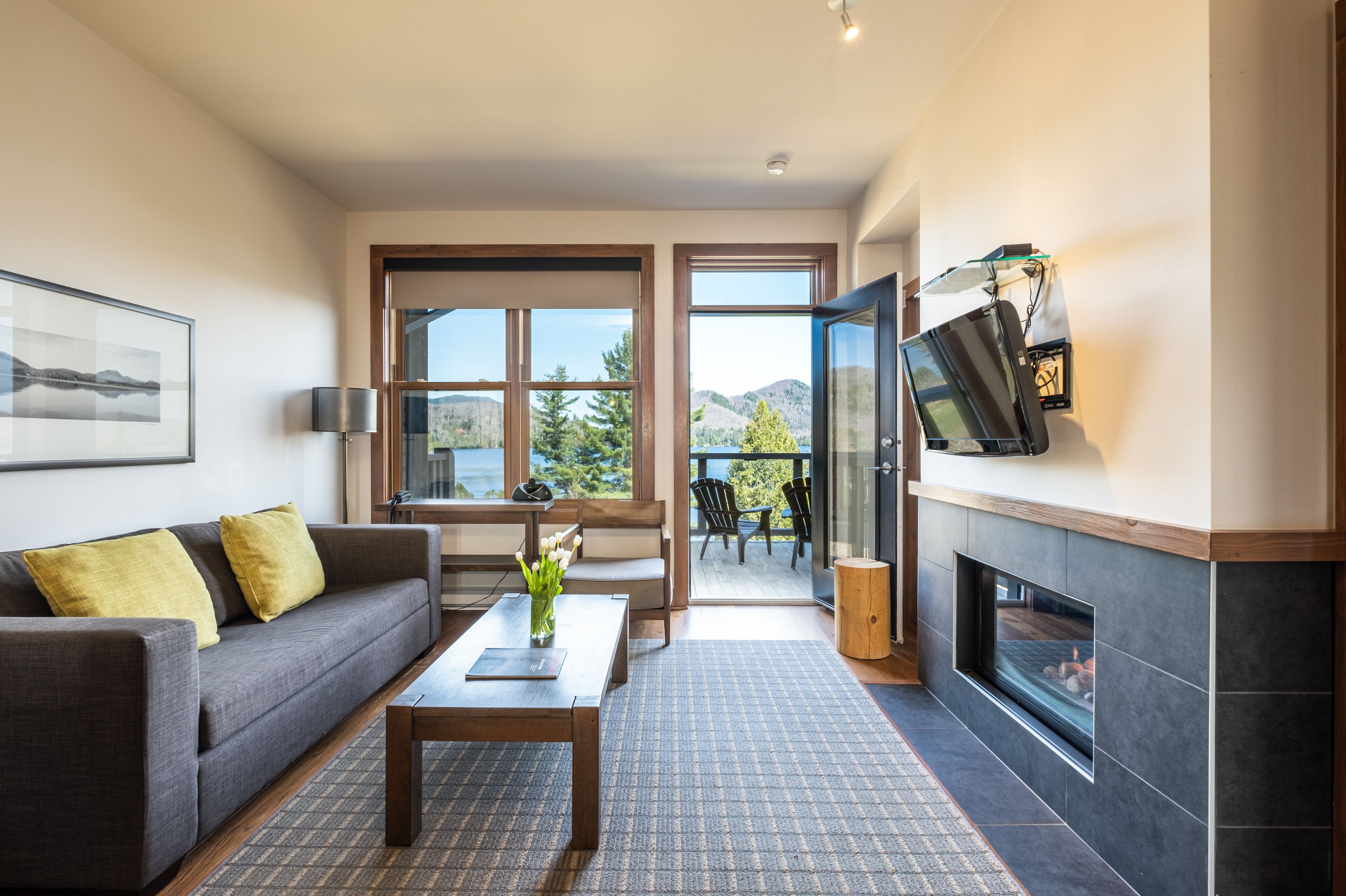A modern living room with a sofa, coffee table, fireplace, and a large window offering a view of the outdoors.