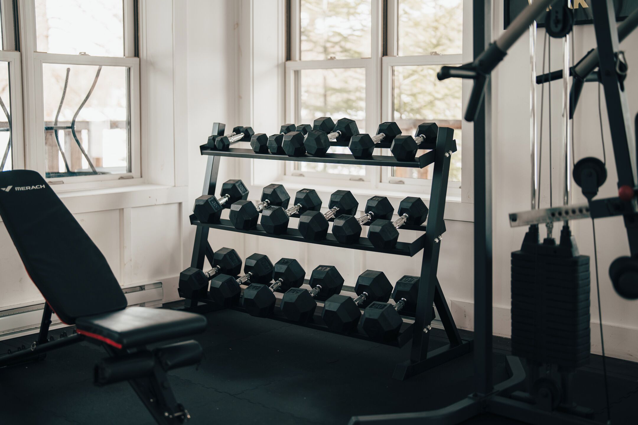 A gym with a bench, dumbbells, and weight machines.