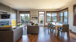 A modern living room with a sofa, coffee table, and dining area with chairs and a table. - Suites Sur Lac (Lac-Superieur)