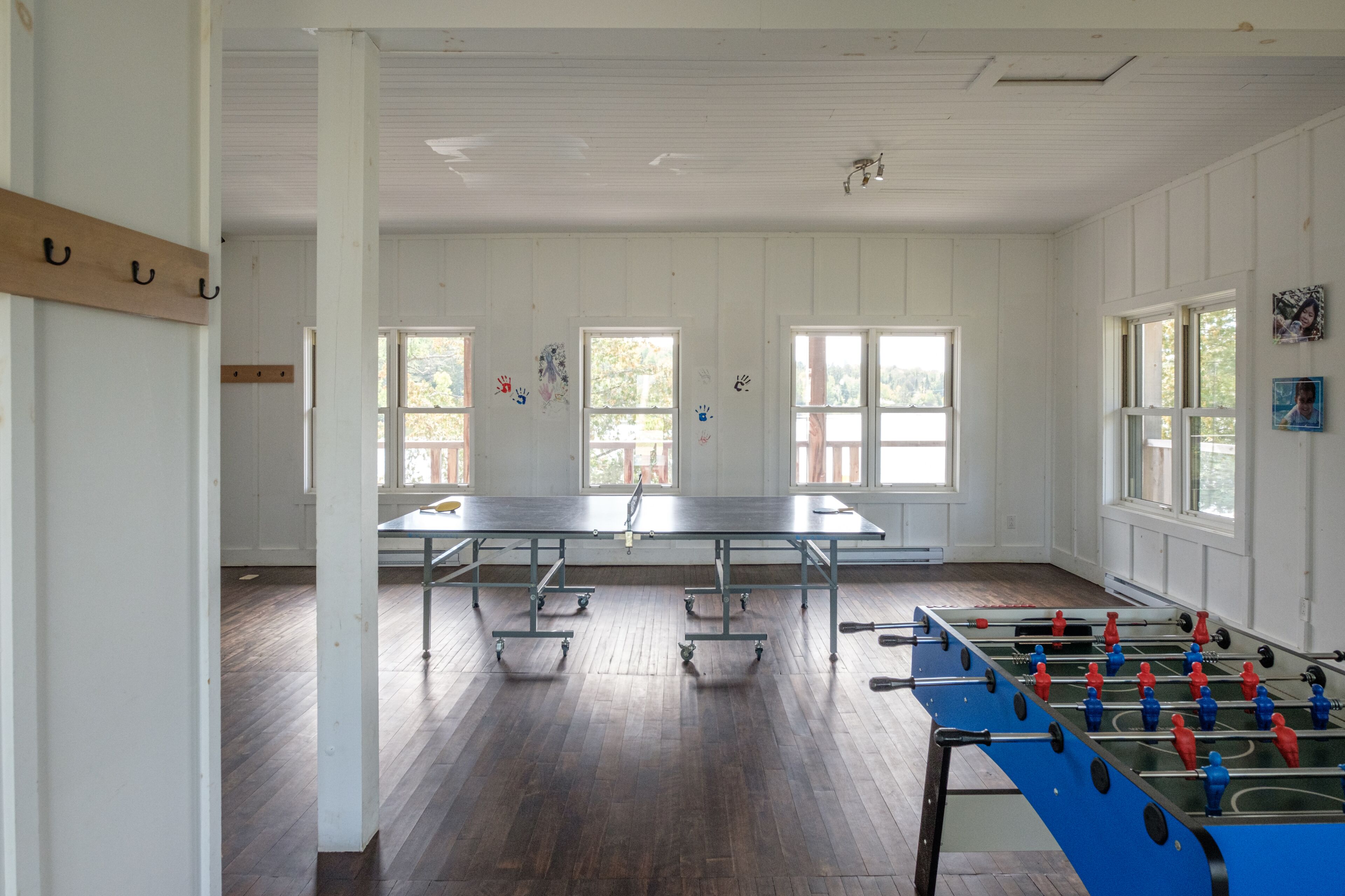 A spacious room with a foosball table, a ping pong table, and large windows allowing natural light.