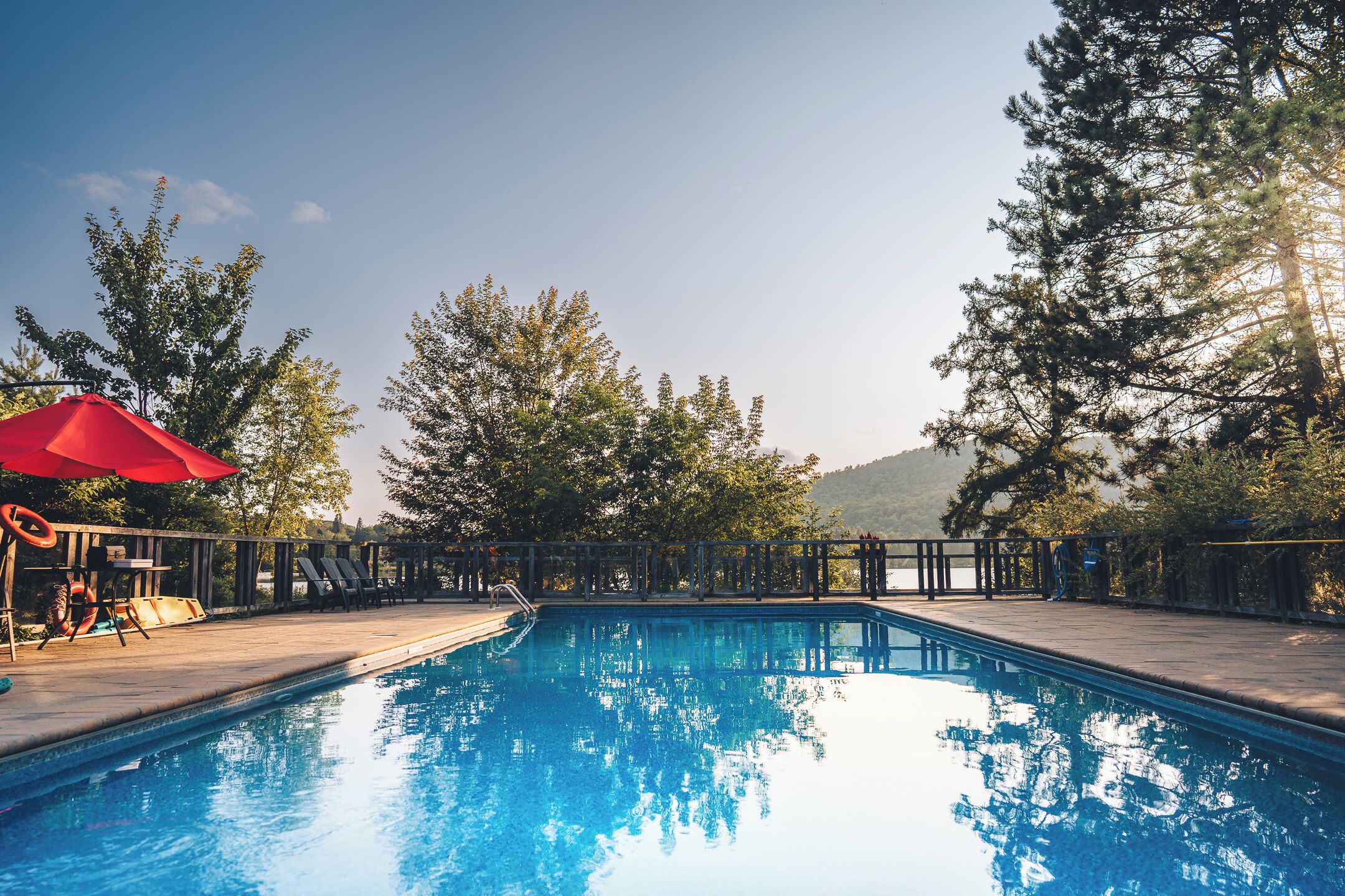 Una piscina con plataforma de madera, rodeada de árboles y una montaña al fondo.