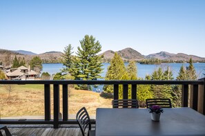 A deck with a table and chairs overlooking a lake with mountains in the background. - Suites Sur Lac (Lac-Superieur)