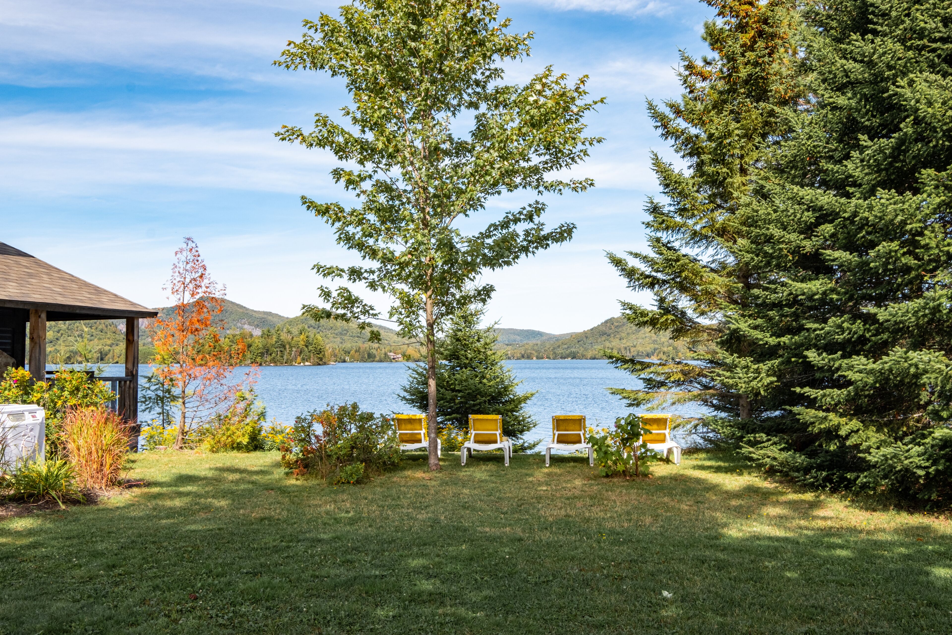 Une vue sur le lac, avec trois chaises disposées face à l’eau, entourées de verdure et d’une structure en bois.