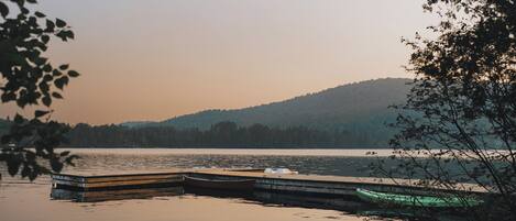 A calm lake with a dock and boats, surrounded by trees and hills in the background.