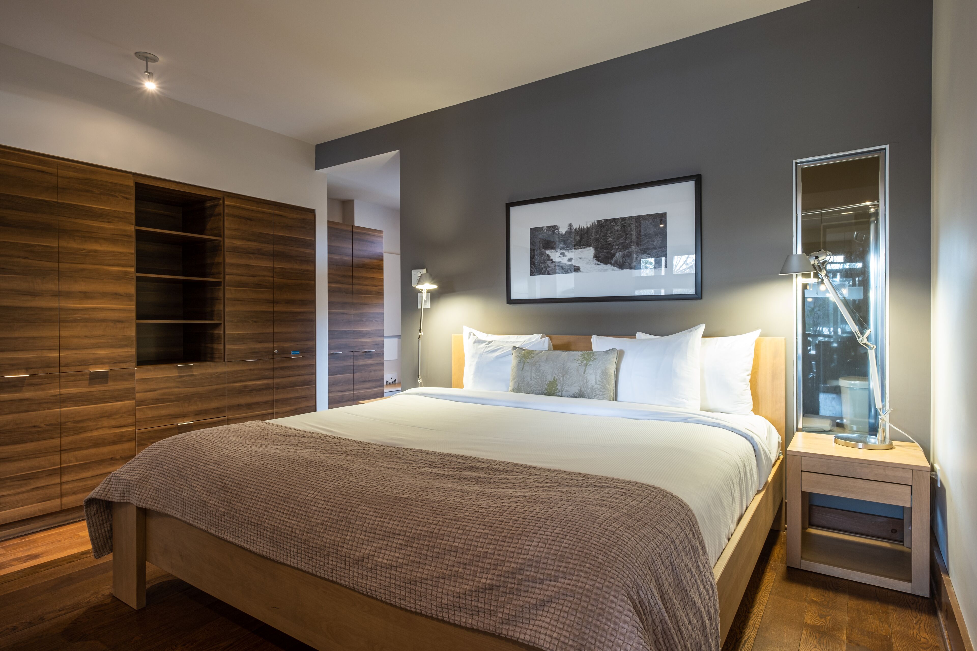 Une chambre à coucher moderne avec un grand lit, une armoire en bois, un tableau encadré au mur et une table de chevet avec une lampe.