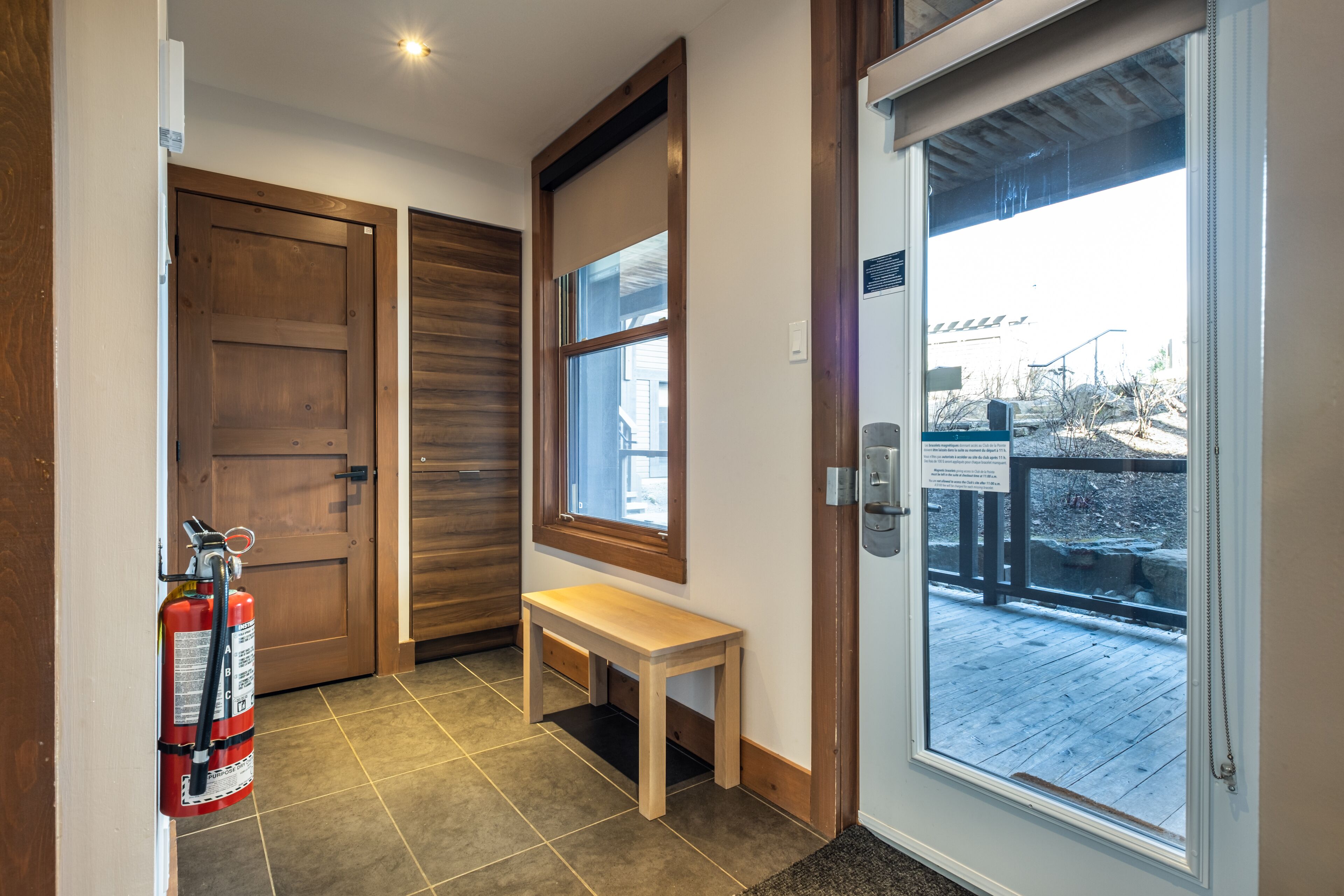 Un pasillo con un banco de madera, un extintor y una puerta que da a un balcón.