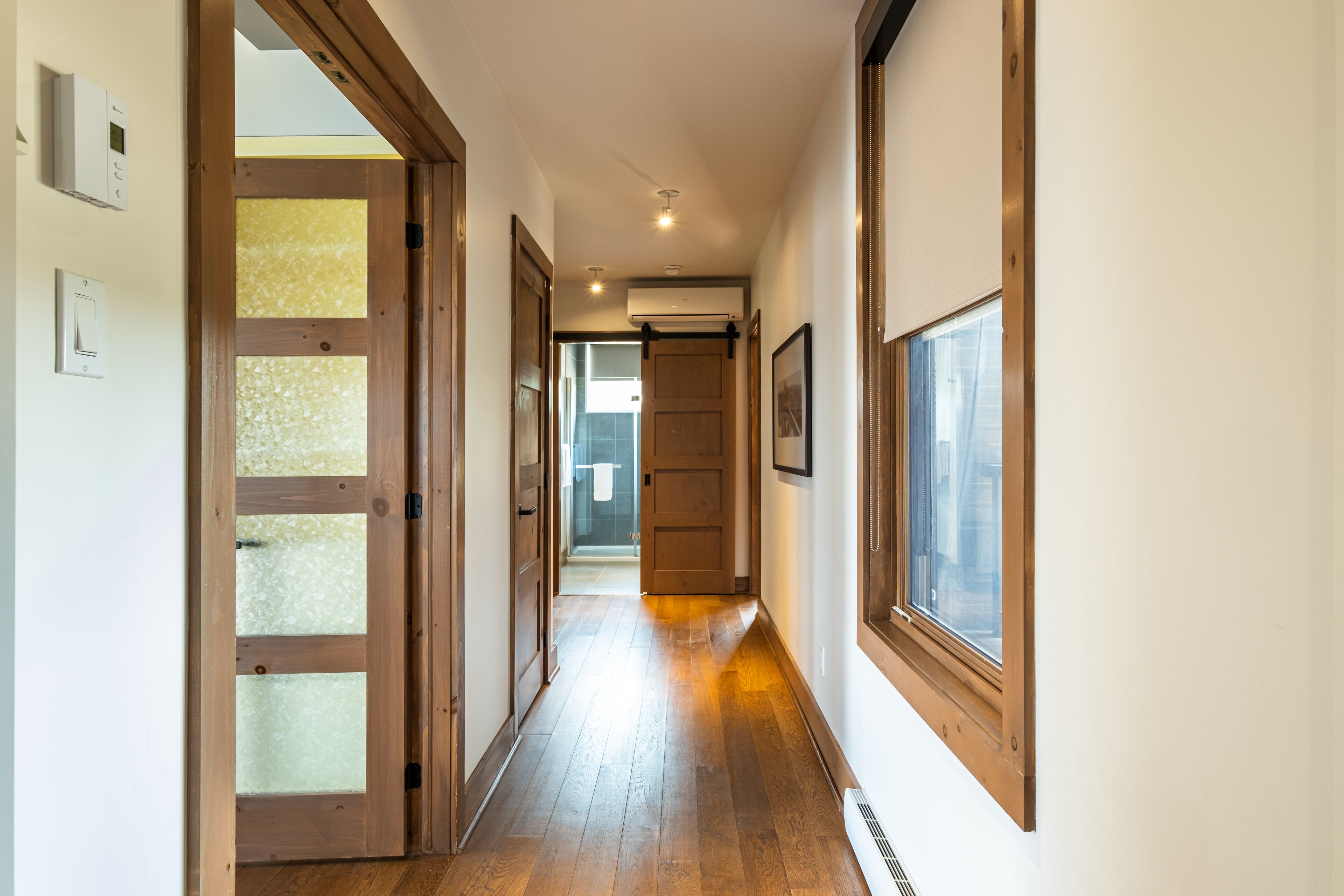 A hallway with wooden doors, a window, and a thermostat.
