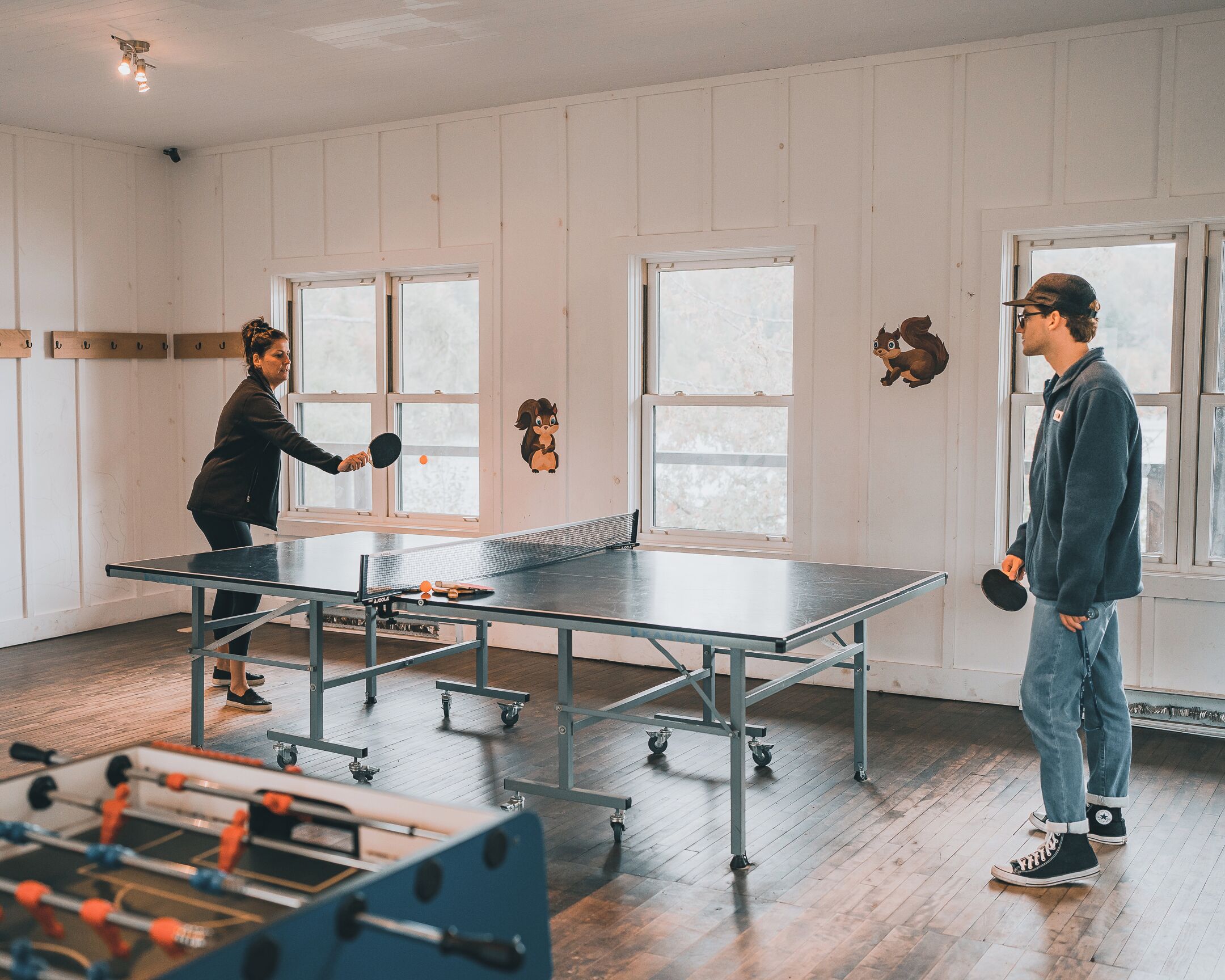 Una mesa de ping pong en una habitación con paredes blancas y ventanas amplias.