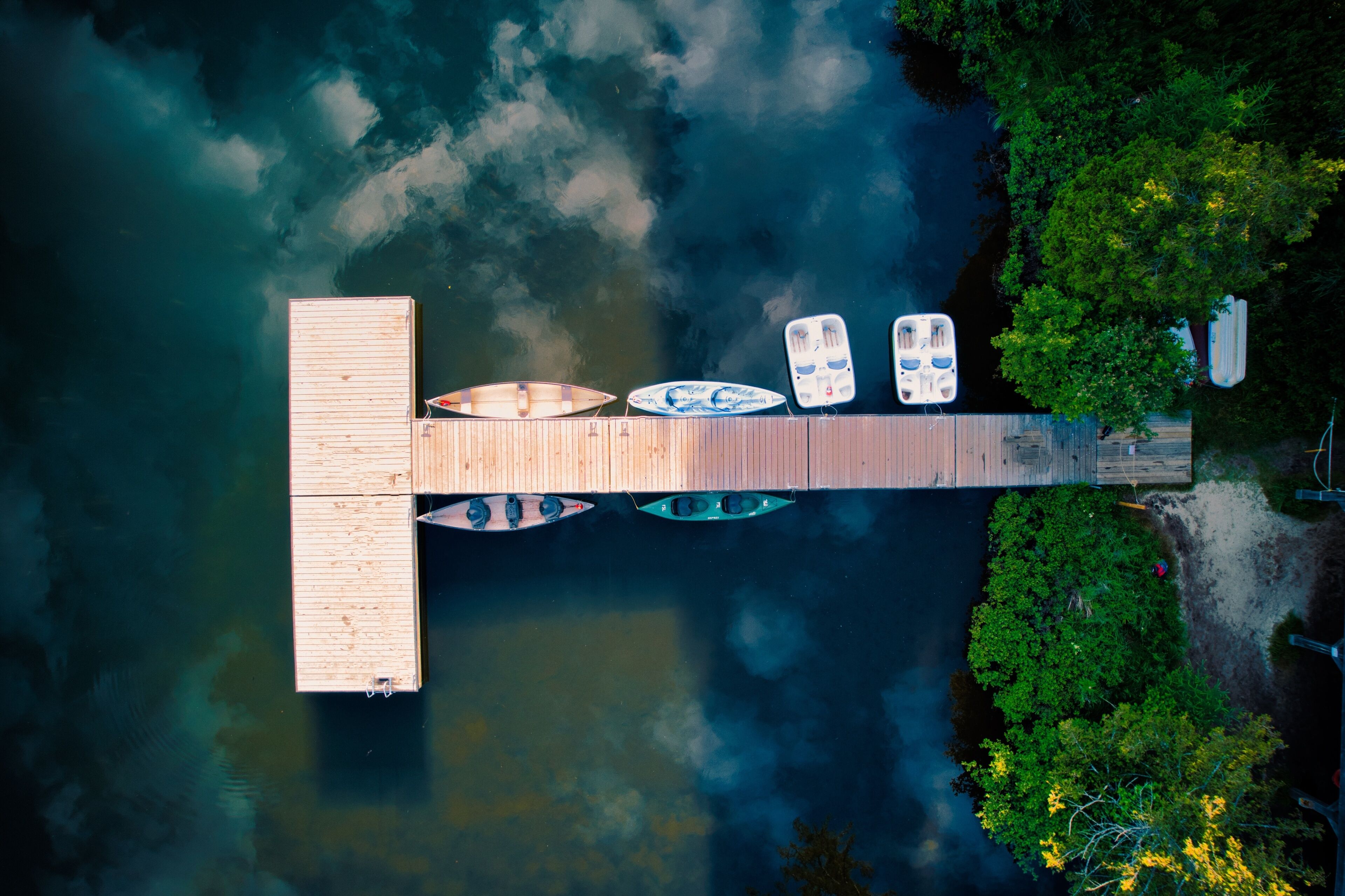 A wooden dock extending into a body of water with several boats moored at the end.