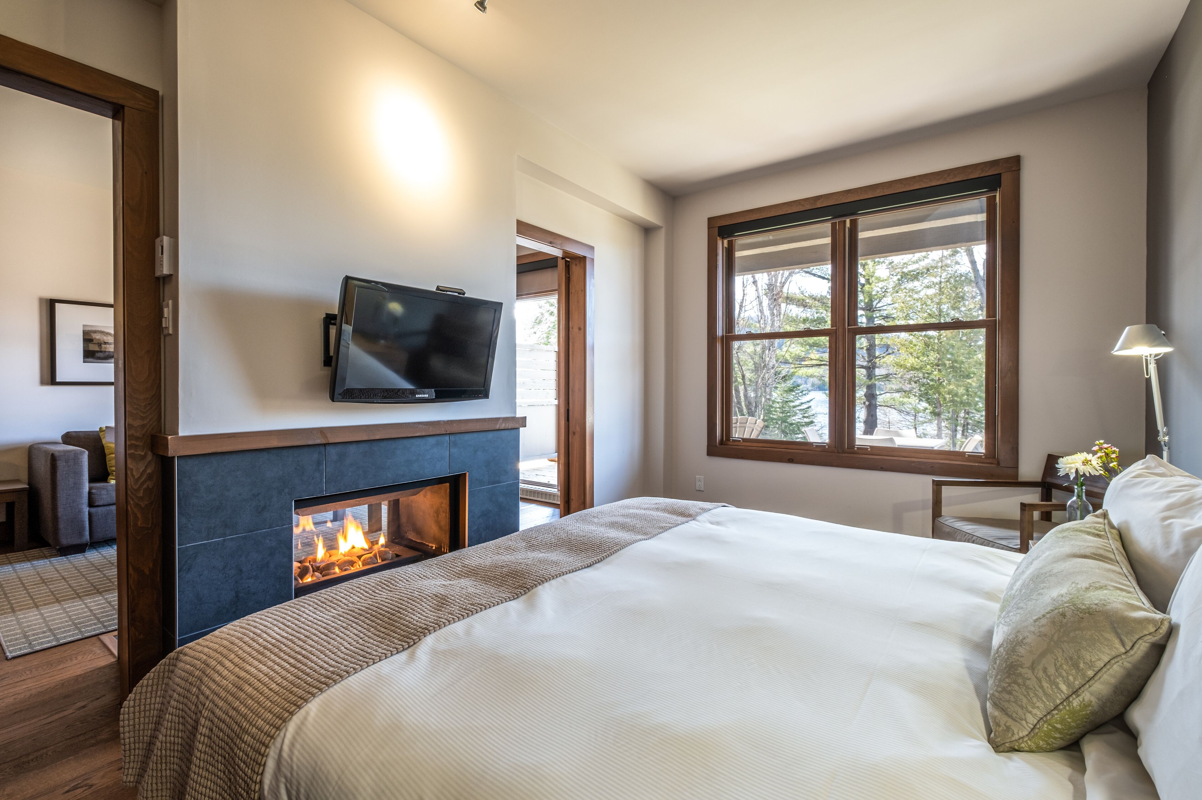 Une chambre dotée d’une cheminée, d’une télévision et d’une grande fenêtre donnant sur les arbres.