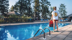 A swimming pool with a metal ladder, surrounded by trees and a clear sky. - Suites Sur Lac (Lac-Superieur)