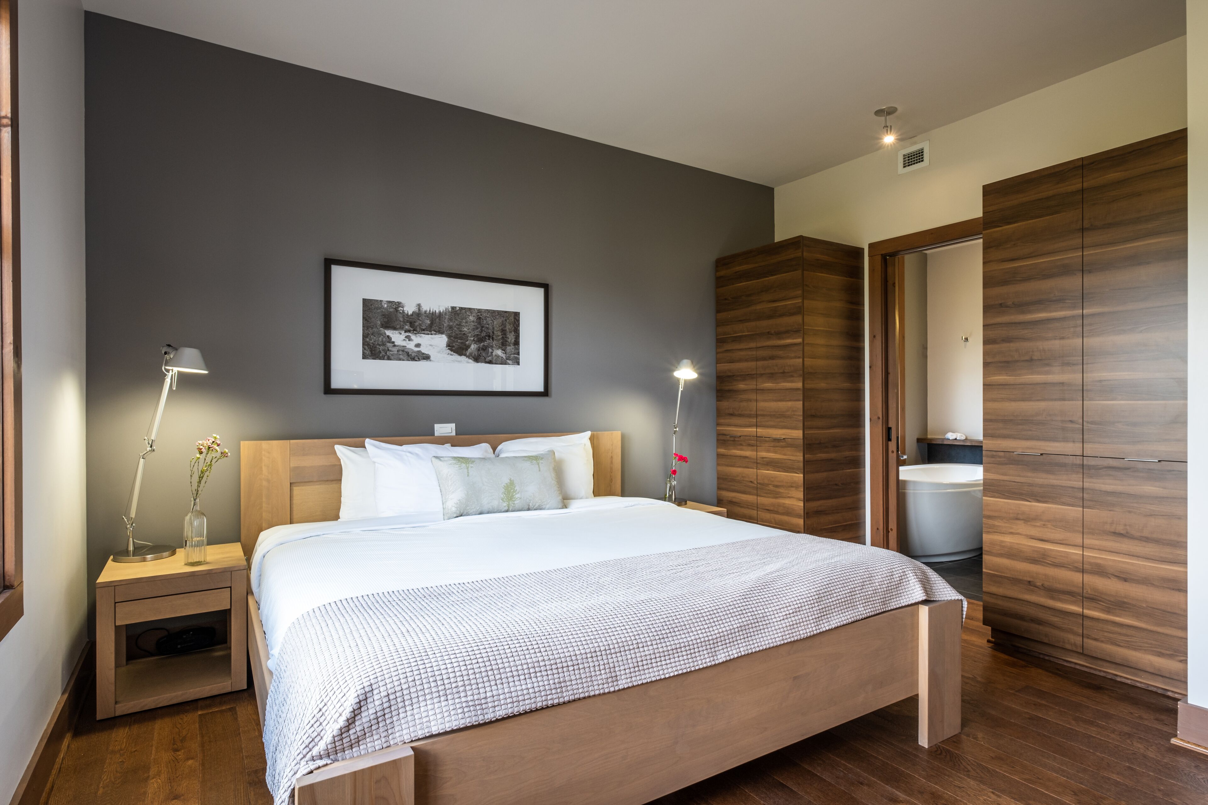 Un dormitorio moderno con una cama de madera, mesitas de noche con lámparas, un cuadro enmarcado en la pared y un armario.