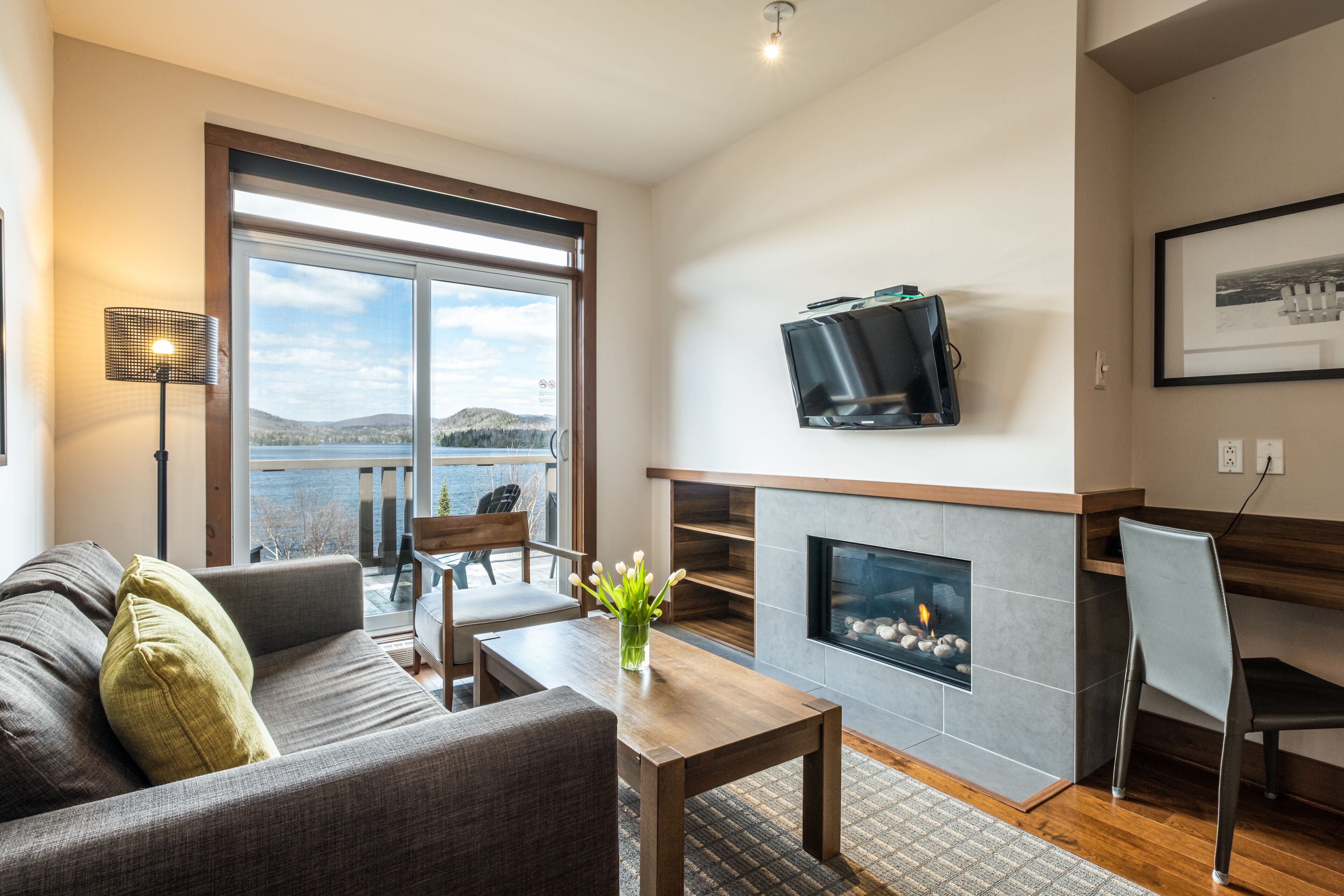 A modern living room with a fireplace, a television mounted on the wall, and a large window offering a scenic view.