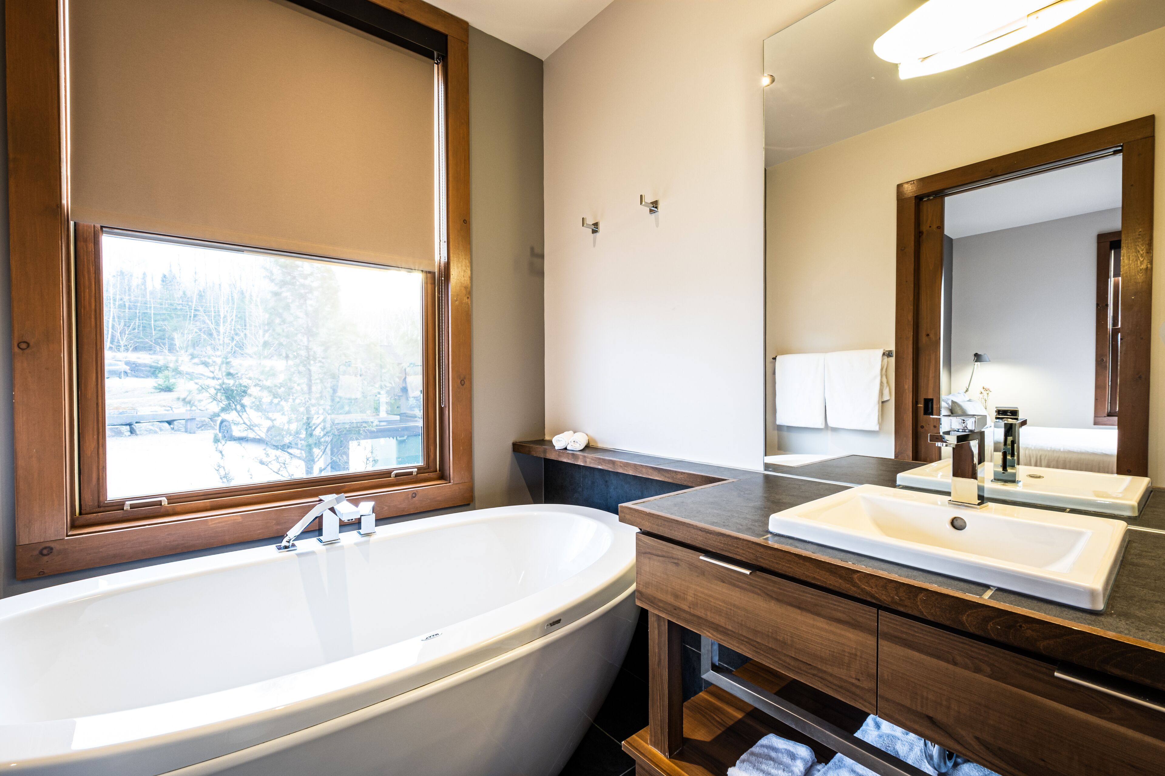 A modern bathroom with a freestanding bathtub, a vanity with a mirror, and a window with a view of trees.