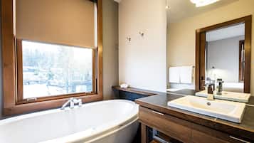 A modern bathroom with a freestanding bathtub, a vanity with a mirror, and a window with a view of trees.