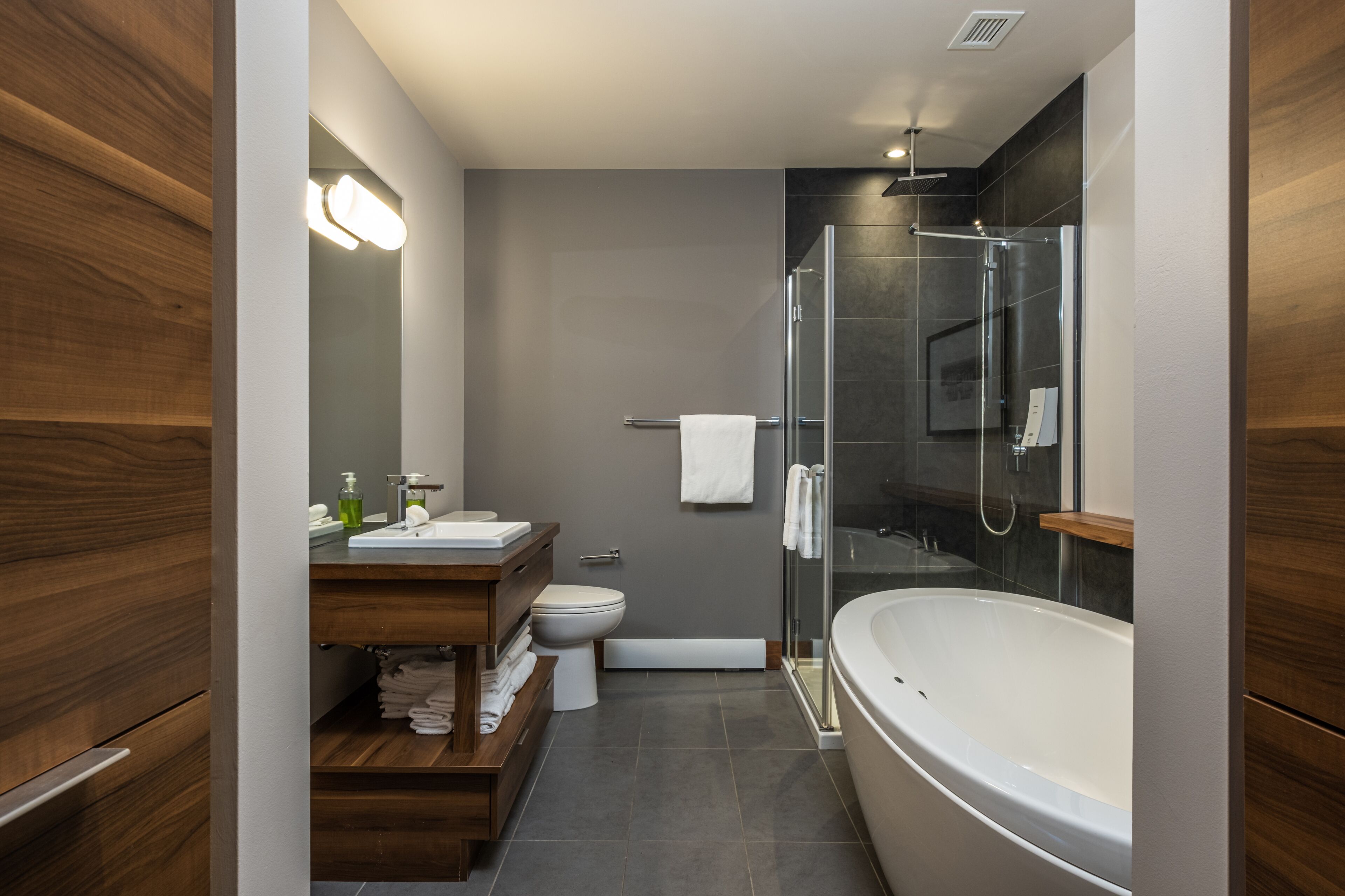 A modern bathroom with a wooden vanity, a white bathtub, and a glass-enclosed shower area.