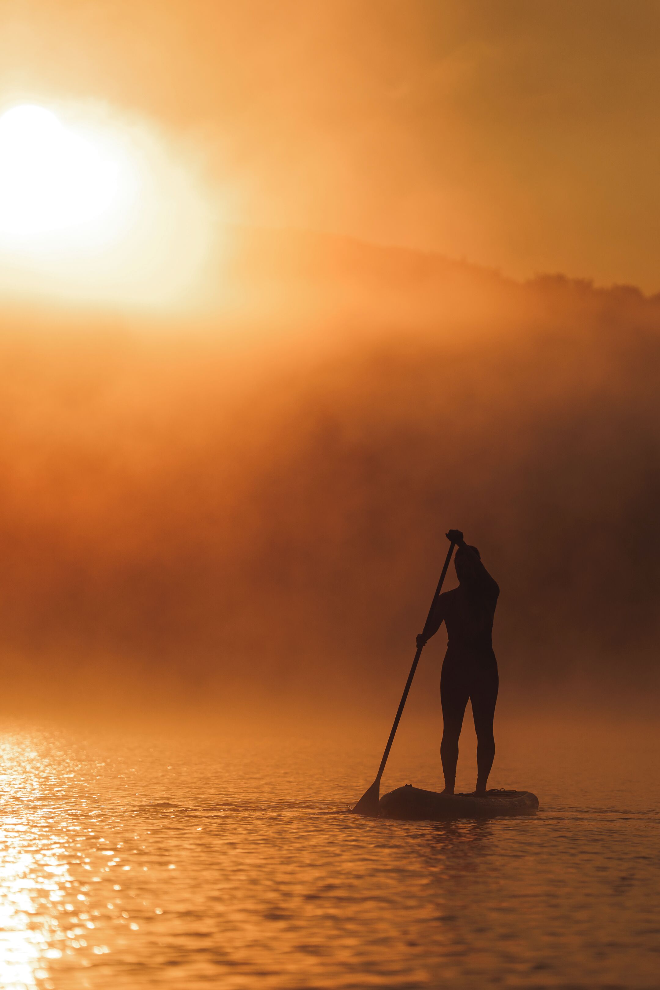 A silhouette of a person paddleboarding at sunset.