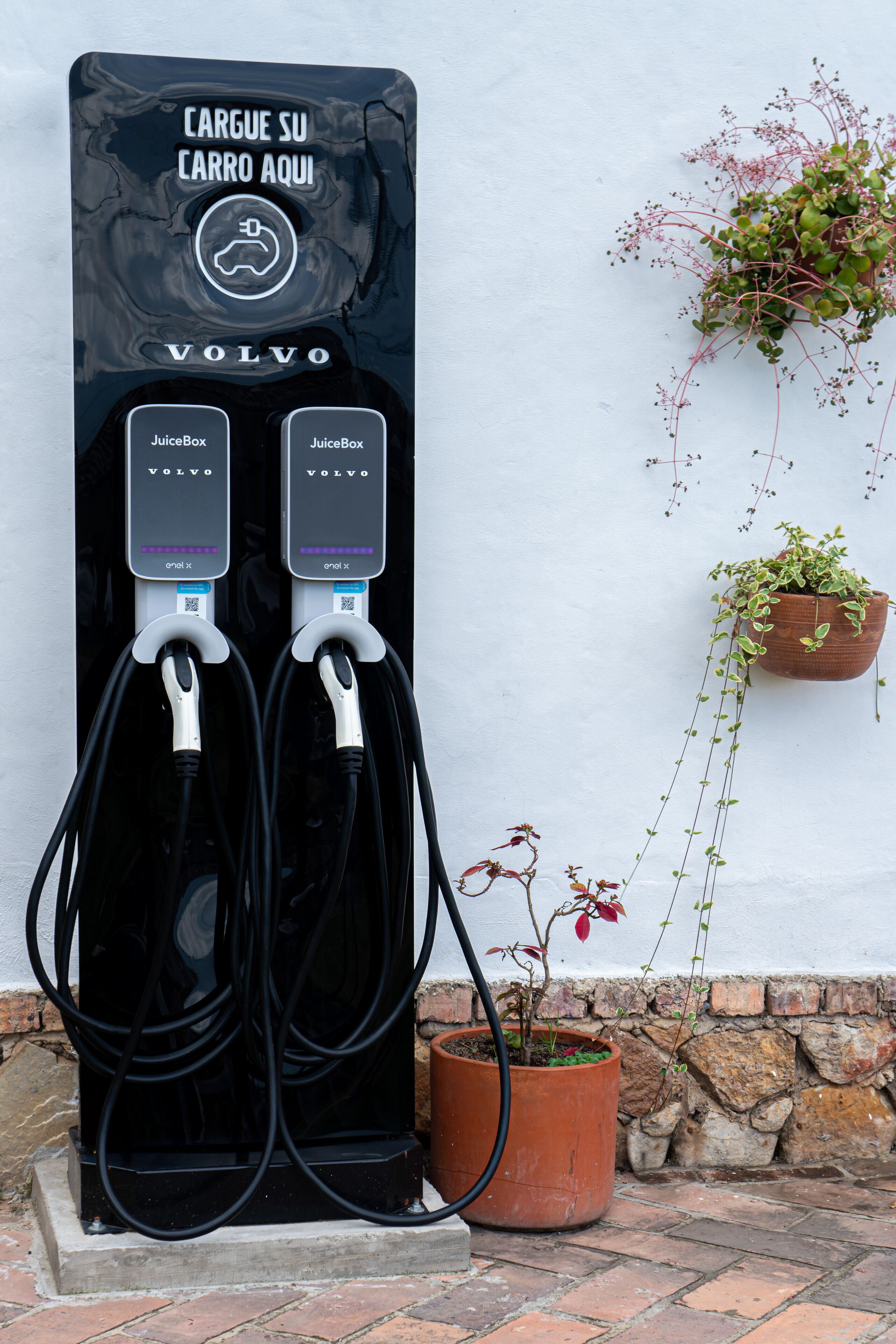 Een zwarte elektrische oplaadpaal met twee laadpunten, gemarkeerd als 'JuiceBox', voor een witte muur.