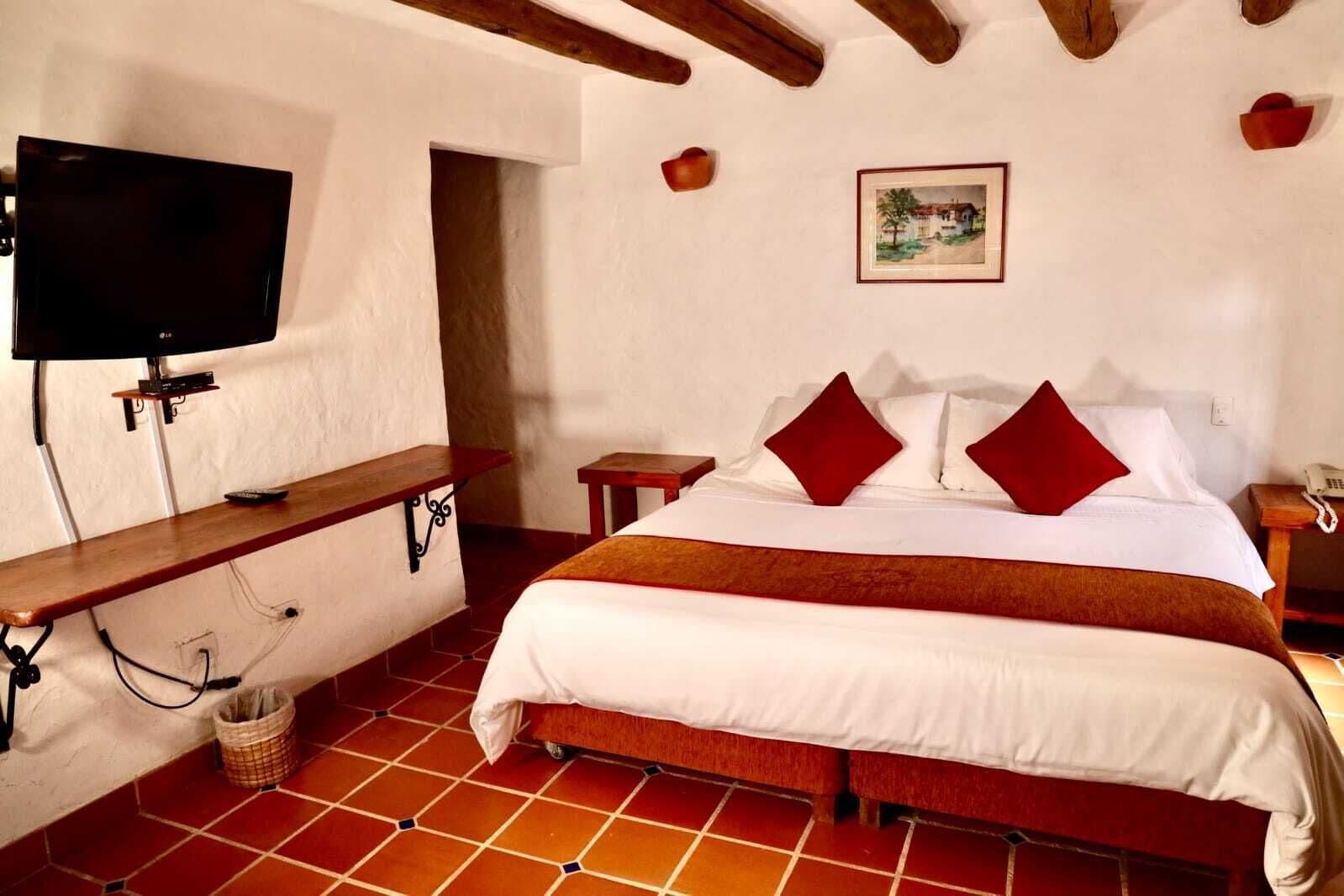 Una camera d'albergo con un letto, una televisione a parete, una panca in legno e un tavolino.
