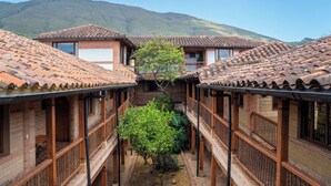 A courtyard with traditional wooden buildings, a central tree, and a mountainous backdrop. - Hotel Plaza Mayor (Villa de Leyva)