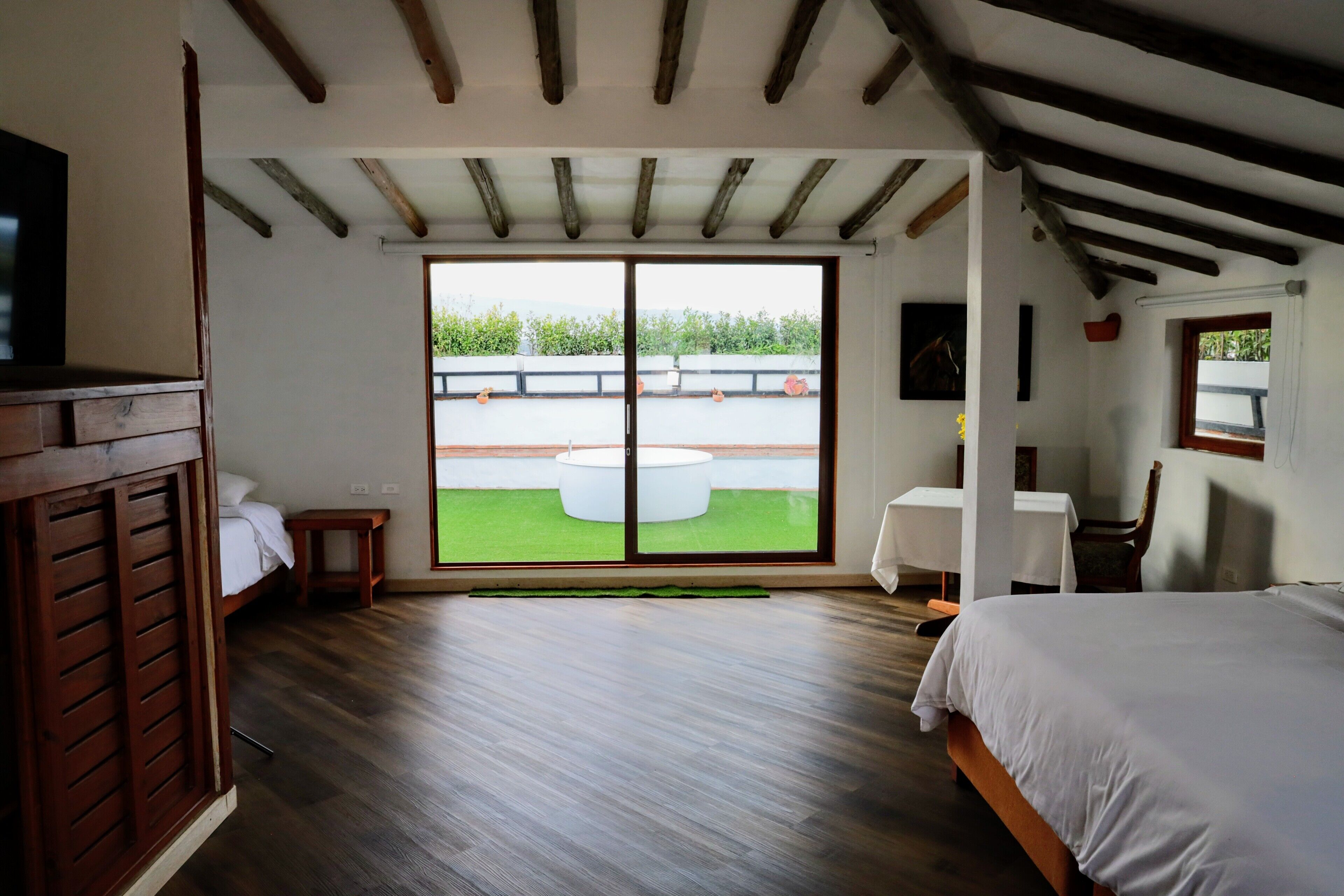 A bedroom with a large sliding glass door leading to a balcony, a bed, a small table, and a chair.