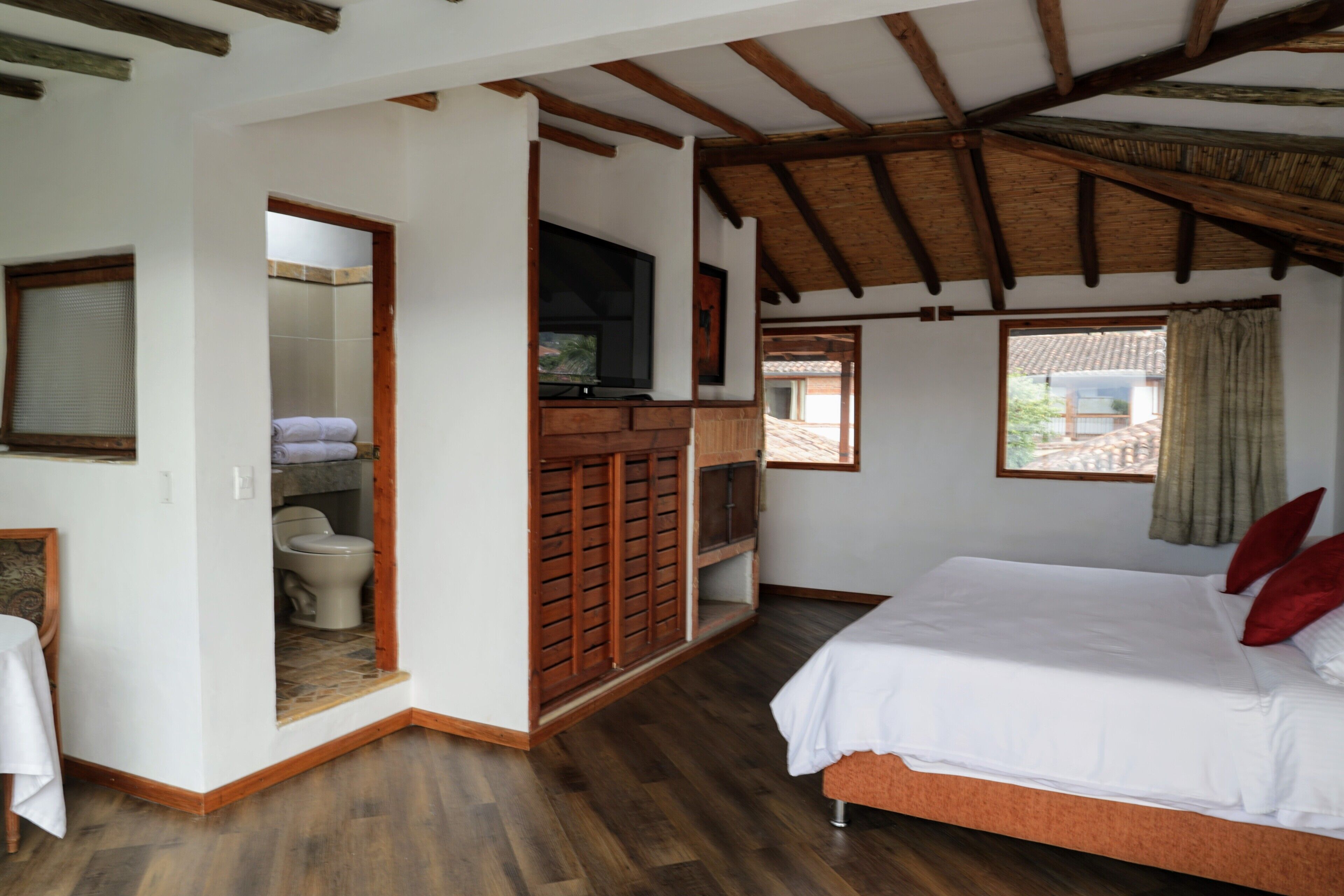 A bedroom with a bed, a television, a wooden wardrobe, and a bathroom visible through an open door.