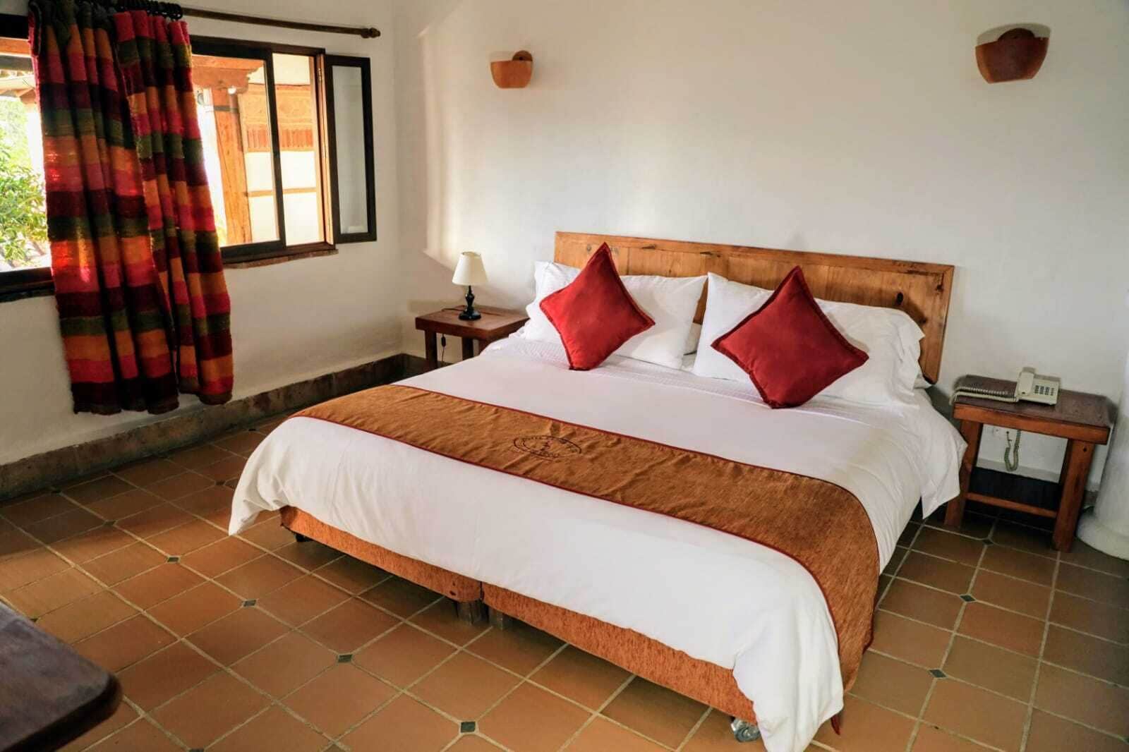 A neatly made bed with a wooden headboard, two bedside tables with lamps, and a window with curtains.