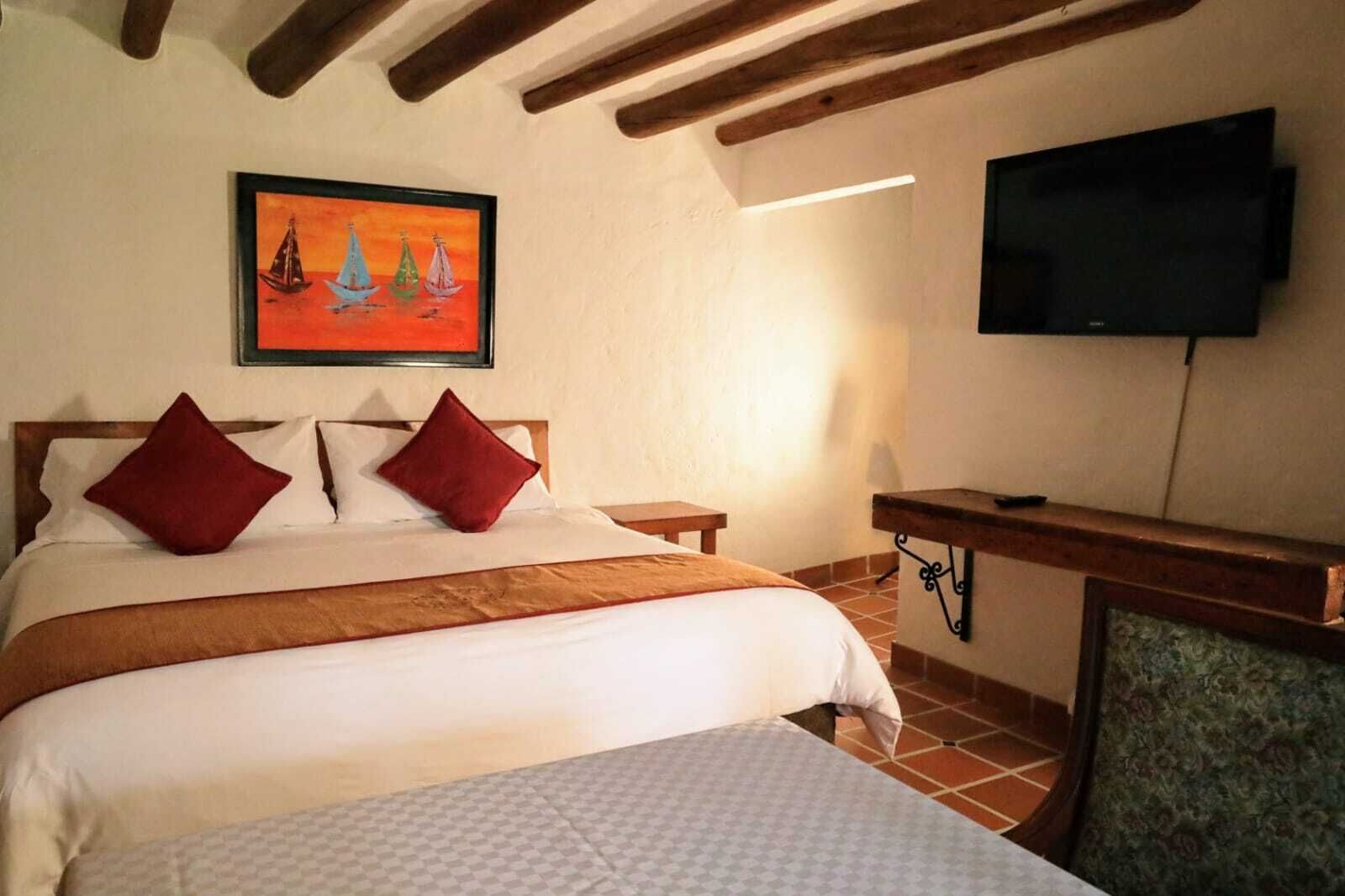 Un dormitorio con una cama, dos almohadas, un cuadro, un televisor y un escritorio.