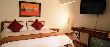 A bedroom with a bed, two pillows, a painting, a television, and a desk.