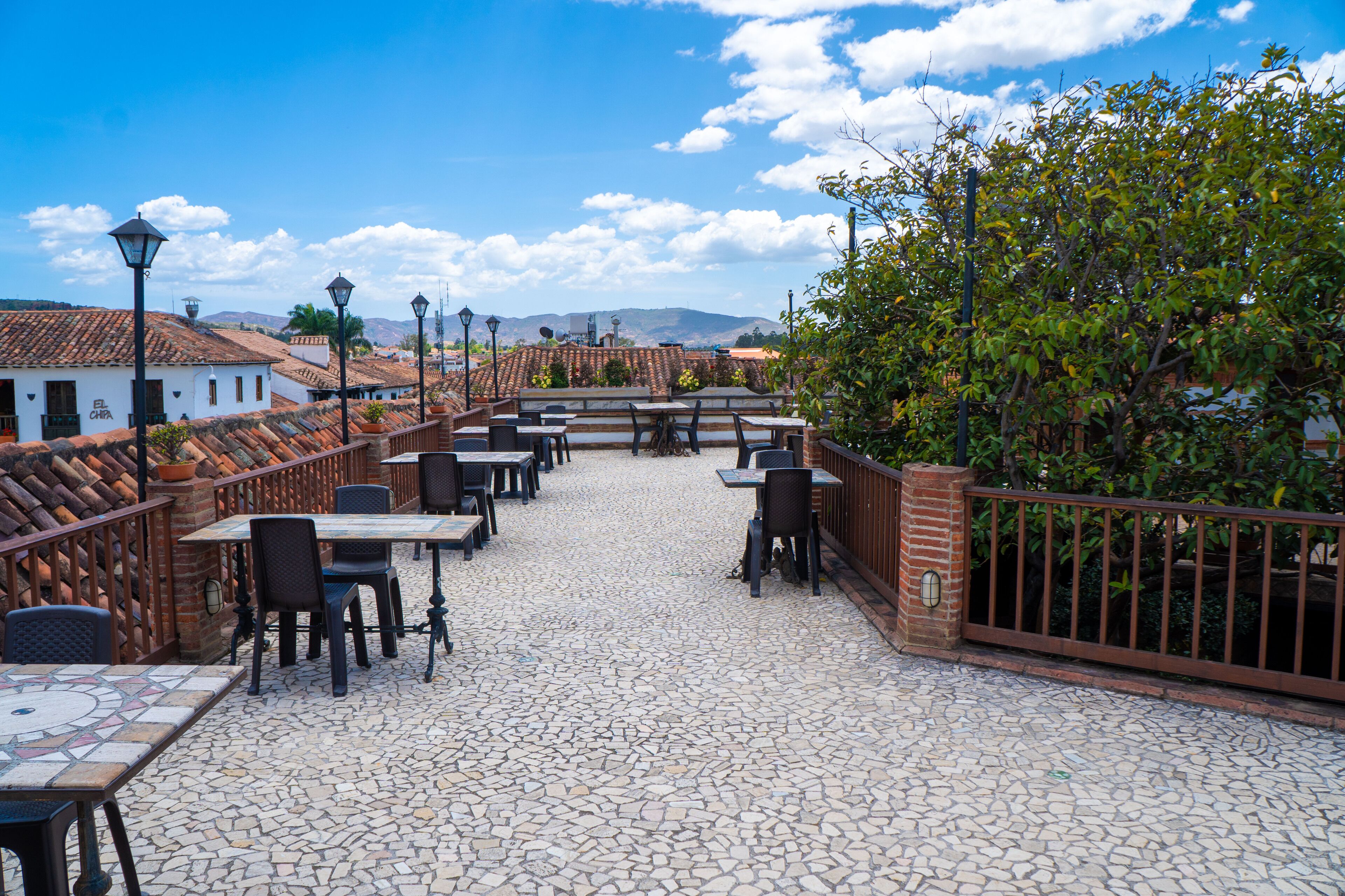 Un patio al aire libre con mesas y sillas, un muro de ladrillo y vistas panorámicas de la ciudad.