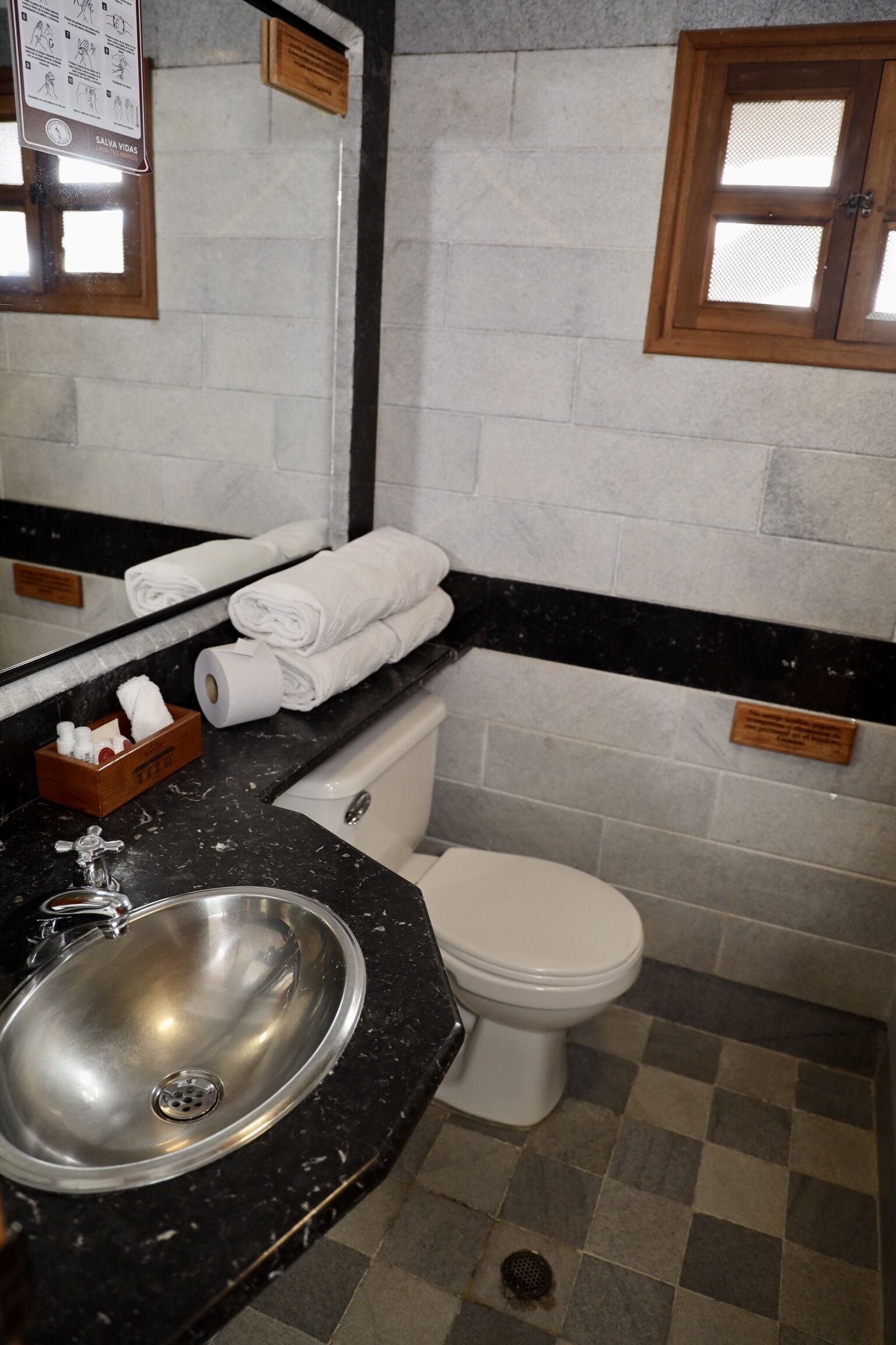 Ein Badezimmer mit Waschbecken, Toilette und Spiegel. Auf der Ablage liegen Handtücher und Pflegeprodukte.