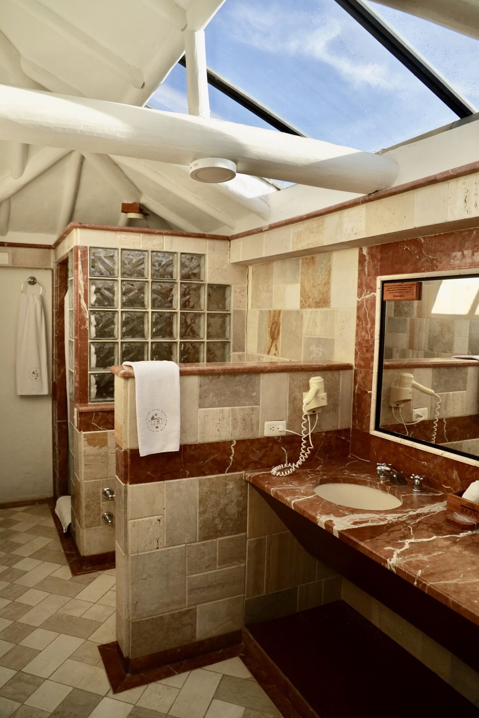 A bathroom with a skylight, marble tiles, a towel rack, a hairdryer, and a mirror.