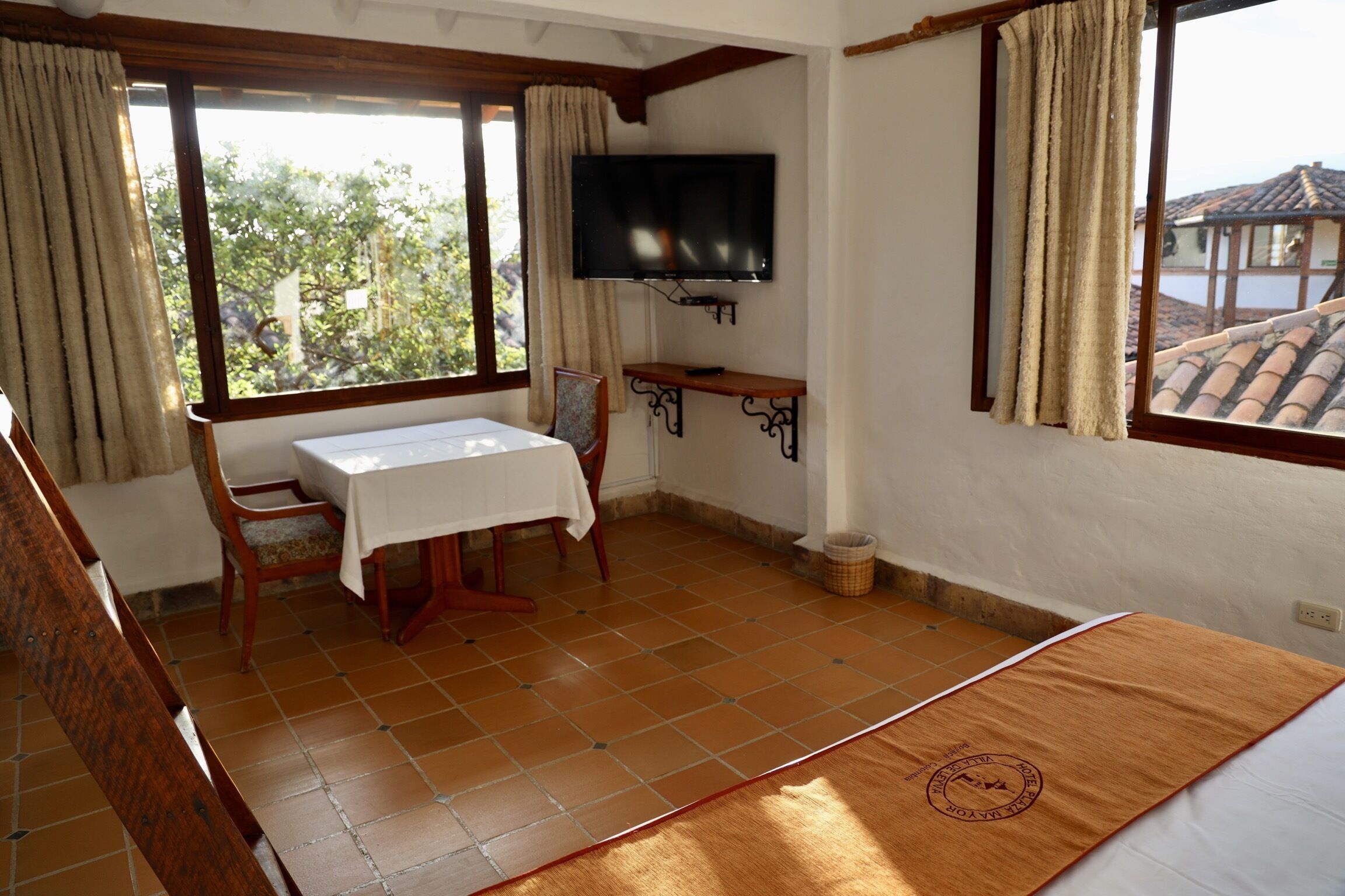 A room with a dining table, chairs, a TV mounted on the wall, and a window with curtains.