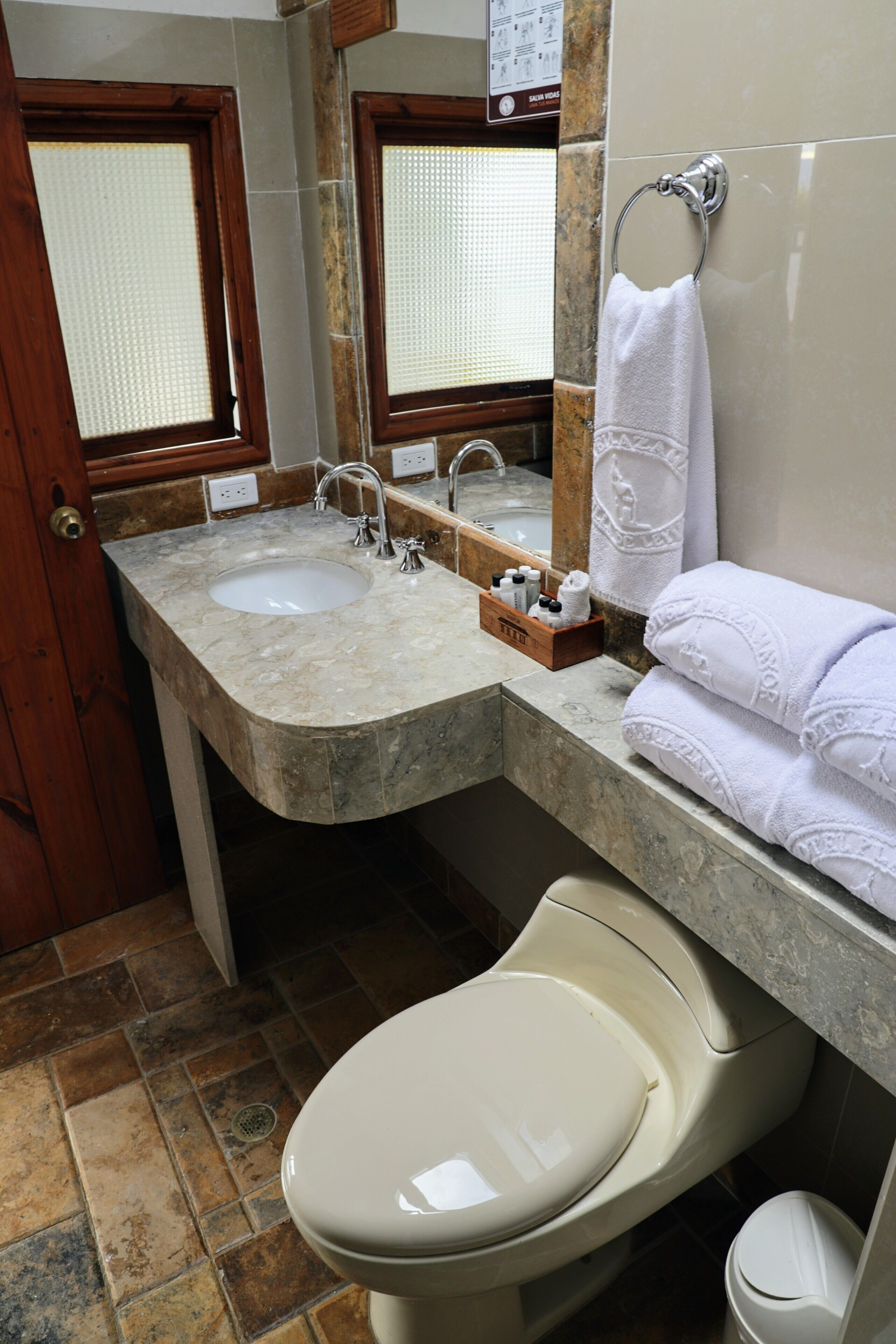 Un baño con lavamanos de mármol, inodoro y espejo.