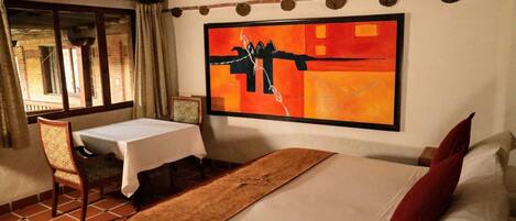 Een hotelkamer met een bed, een tafel en een stoel. Er is een raam met gordijnen en een schilderij aan de muur.