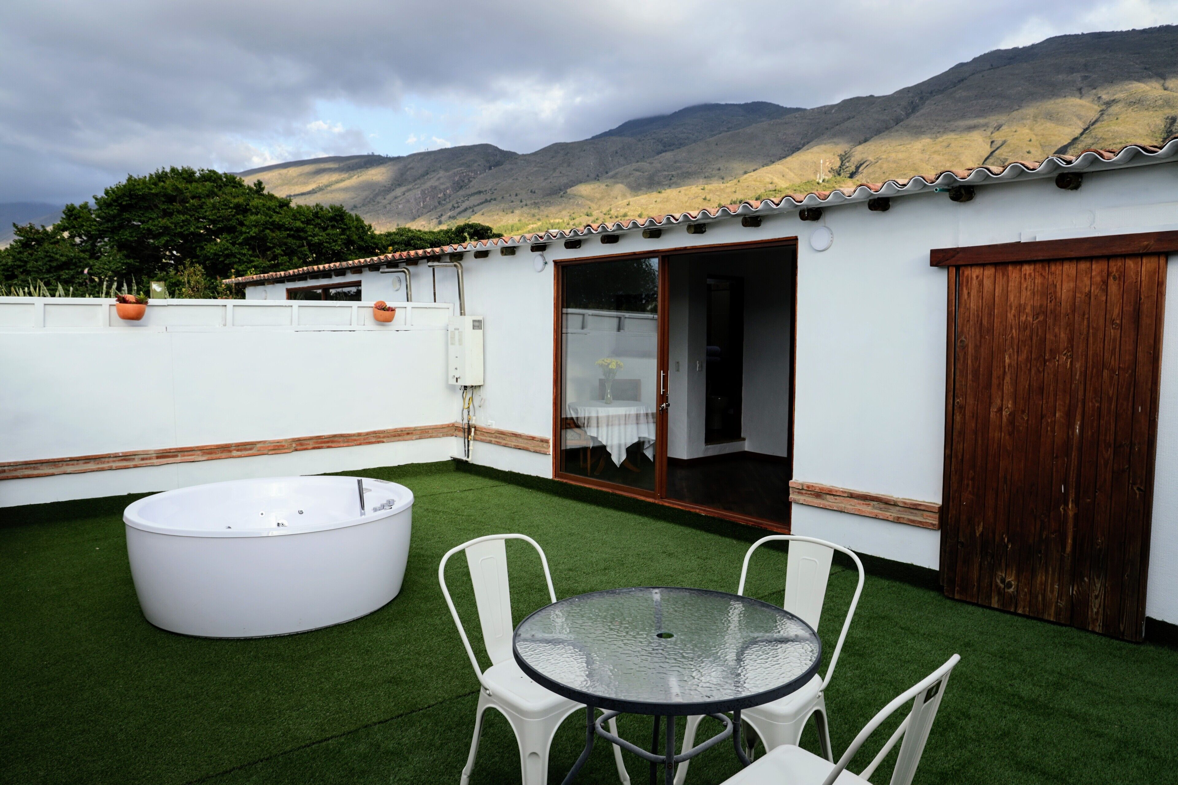 A rooftop patio with a glass table and chairs, a hot tub, and a view of mountains.