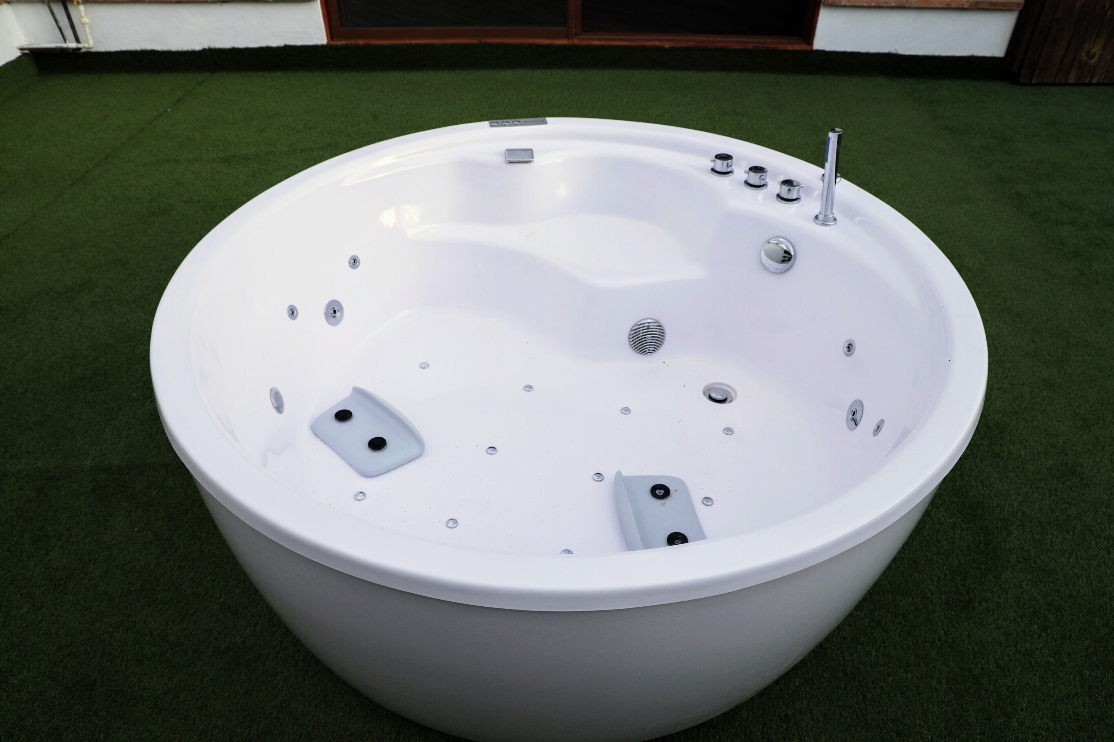 Un grand jacuzzi blanc, autonome, doté de plusieurs jets et d’un panneau de commande, installé sur une pelouse artificielle.