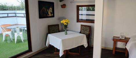 Una habitación con una mesa de comedor, sillas, un jarrón con flores amarillas, un cuadro y vistas al exterior.