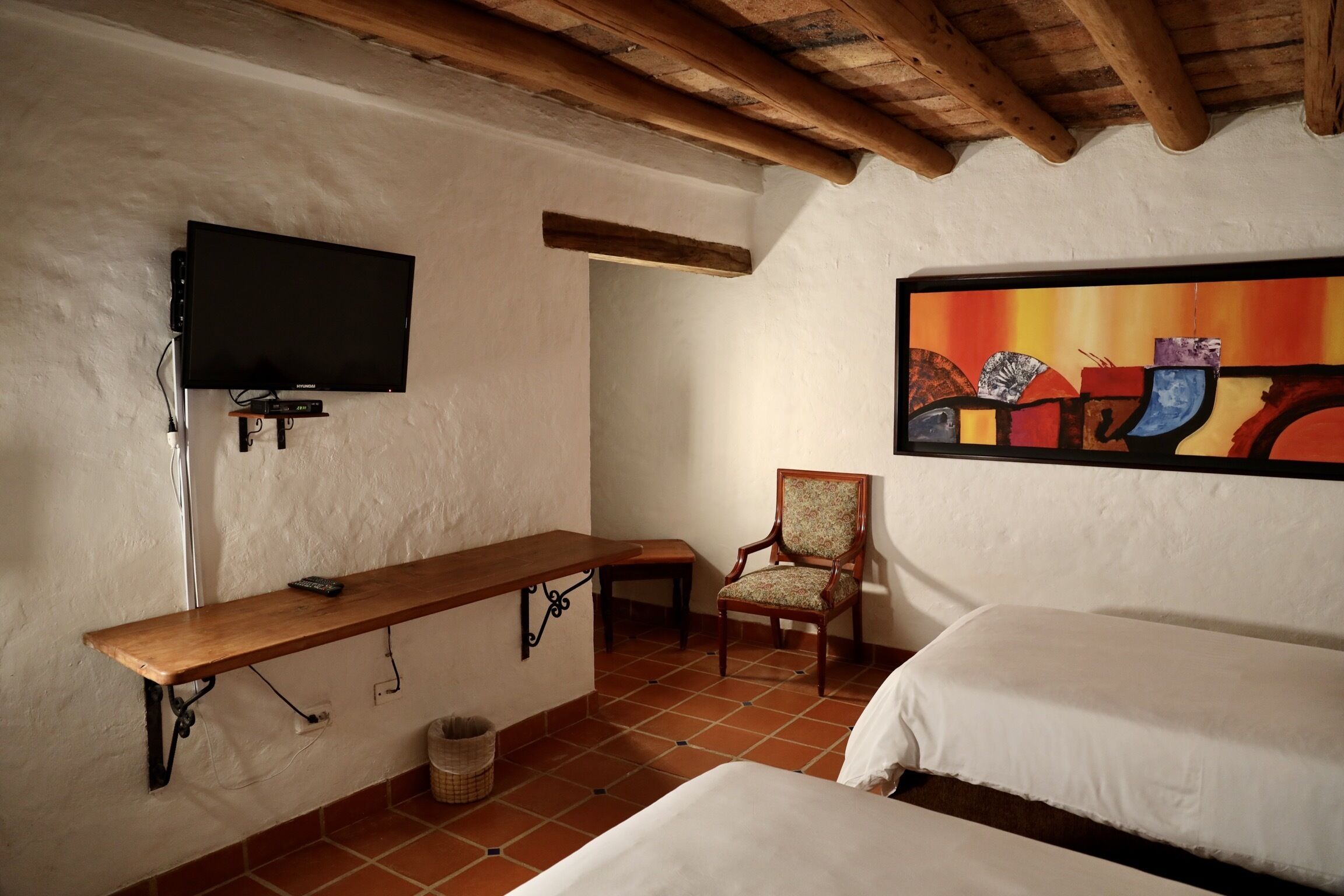 A room with a bed, a chair, a TV mounted on the wall, and a painting.