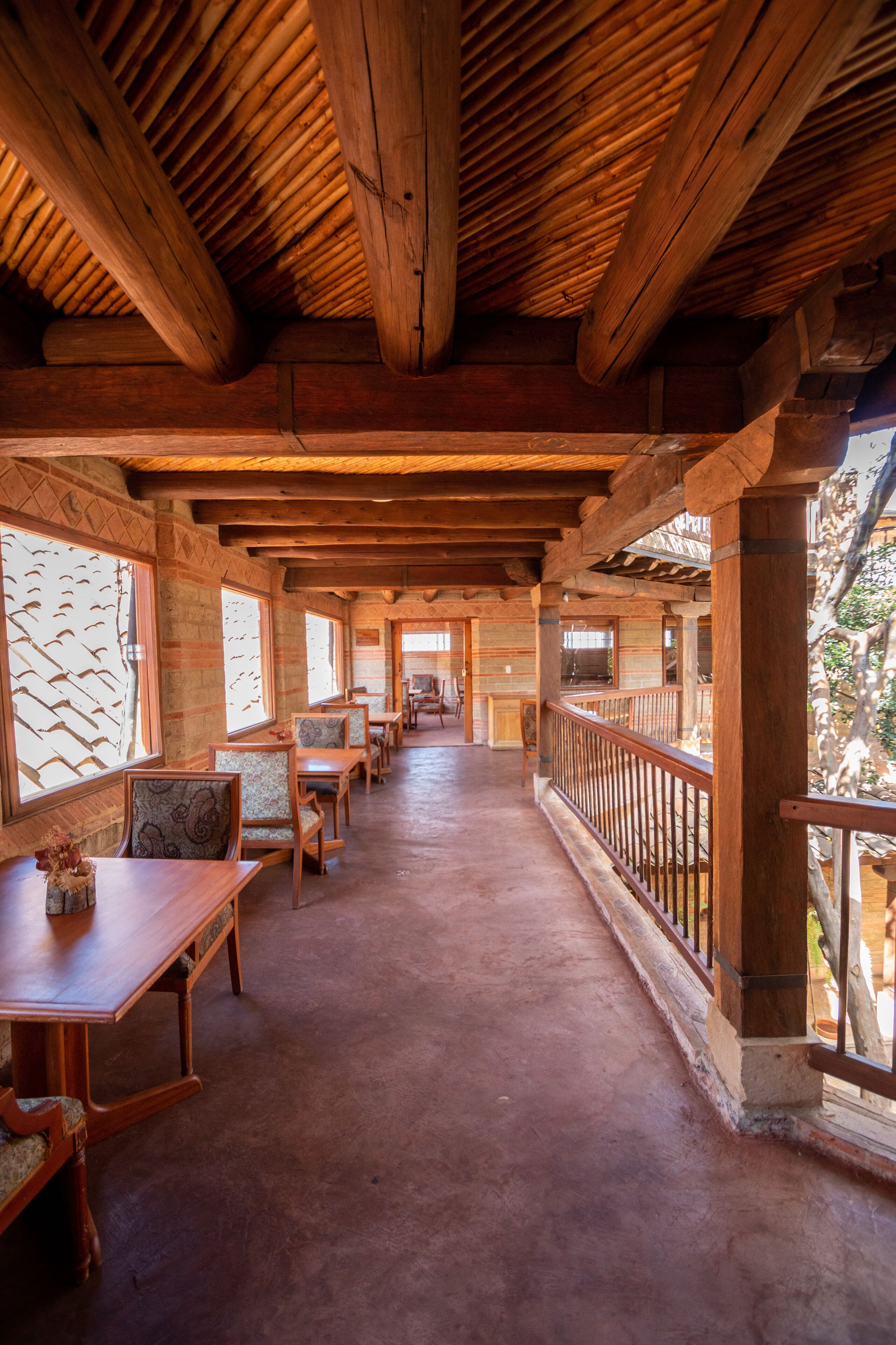 A wooden interior with a long corridor, wooden tables, chairs, and a balcony with a railing.