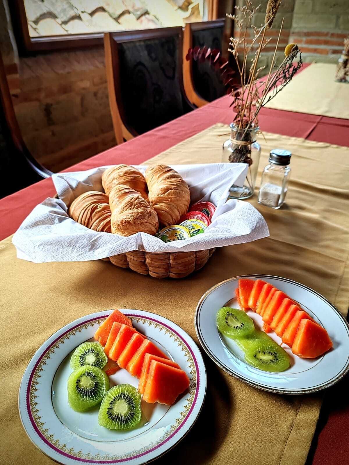Une table dressée avec des croissants, un panier de pain et des assiettes de kiwis et de pastèques coupés en tranches.