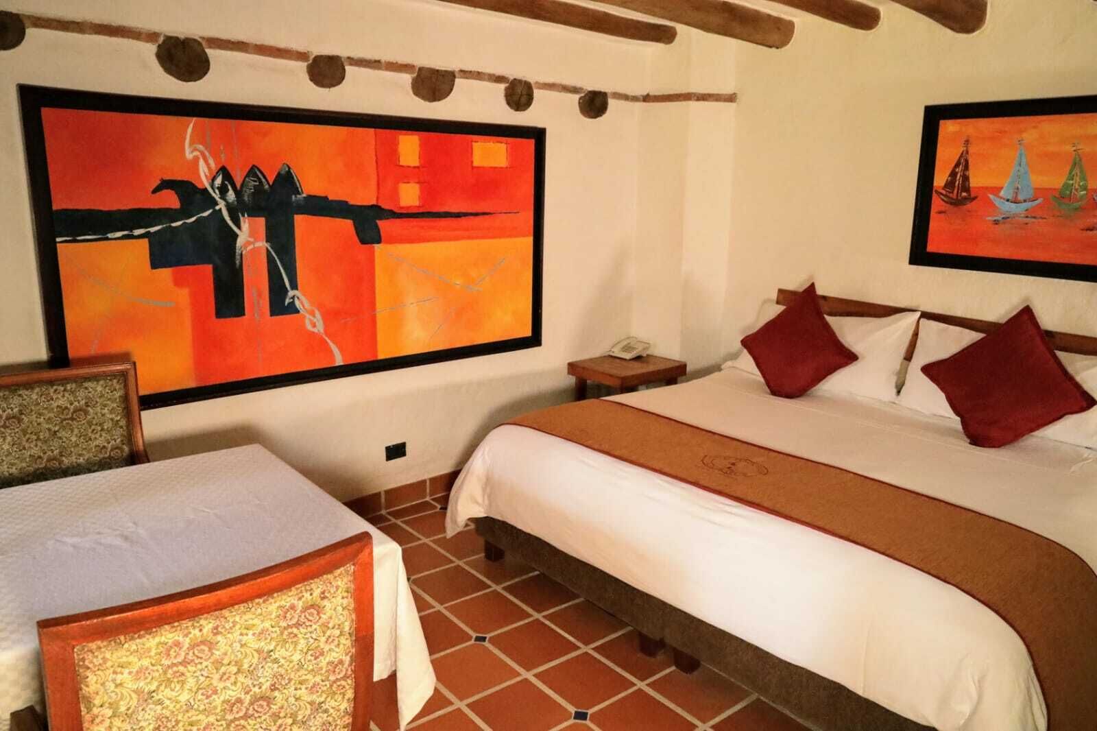 A hotel room with a large bed, a smaller bed, a chair, a nightstand, and a painting on the wall.