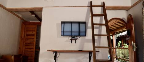 A room with a loft bed, a wooden ladder, a television mounted on the wall, and a small table.