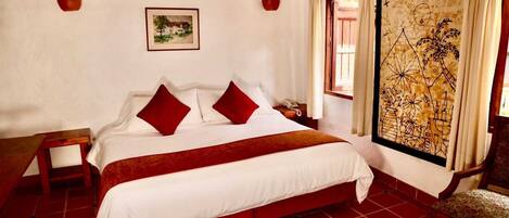 A bedroom with a large bed, red and white bedding, a nightstand, a telephone, a window with curtains, and a wall painting.