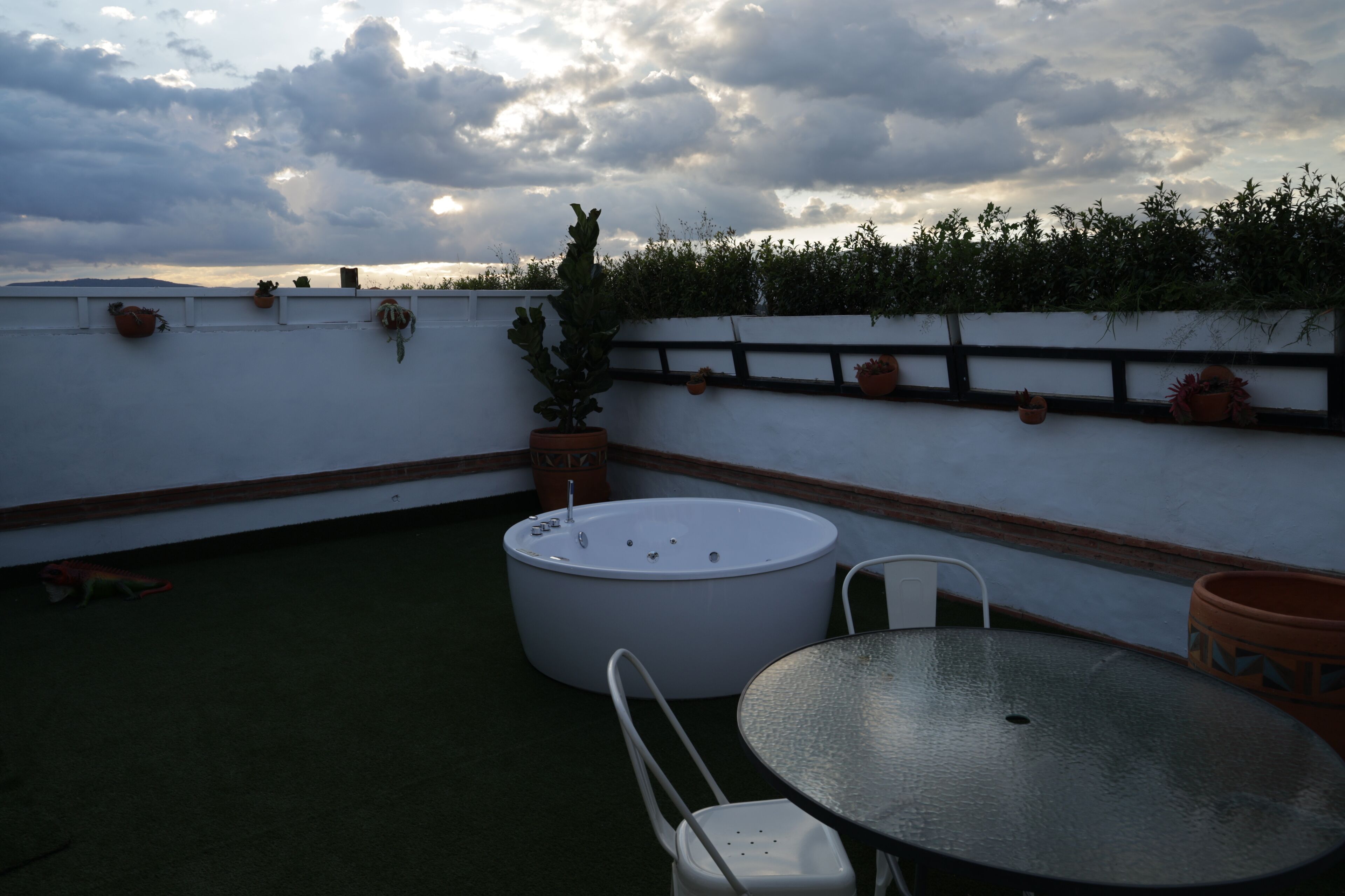 Una terrazza sul tetto con un tavolo rotondo e sedie, una grande vasca da bagno bianca e diverse piante in vaso.